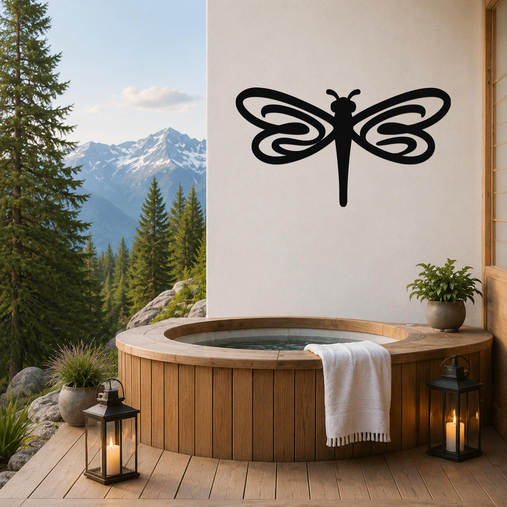 Black metal dragonfly wall art with flowing wing cutouts, mounted on a white wall above a wooden hot tub on a mountain-view deck.