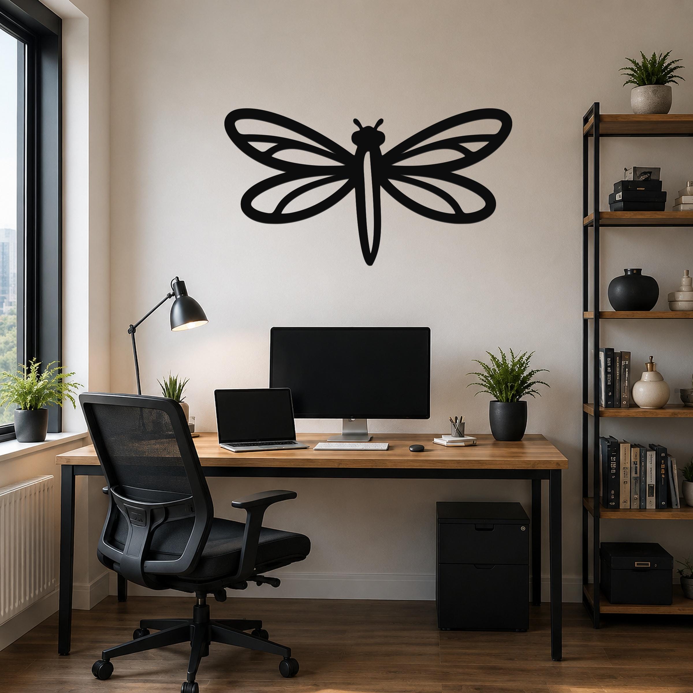 Black metal dragonfly wall art with intricate wing cutouts, mounted on a light-colored wall above a wooden desk in a home office.