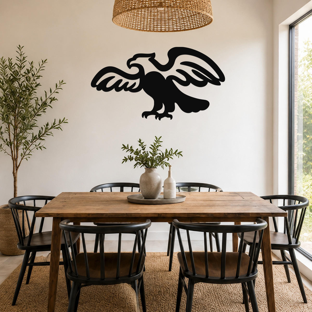 Black metal eagle wall art with outstretched wings and detailed feather cutouts, mounted on a white wall above a wooden dining table in a bright dining room.