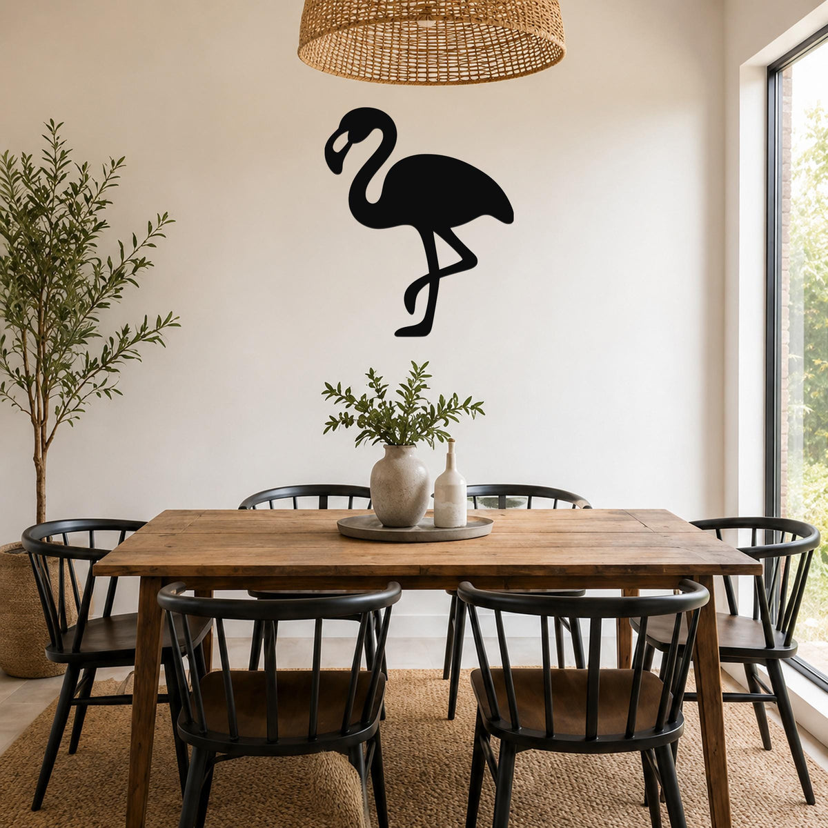 Black metal flamingo wall art silhouette mounted on a white wall above a wooden dining table in a bright dining room.