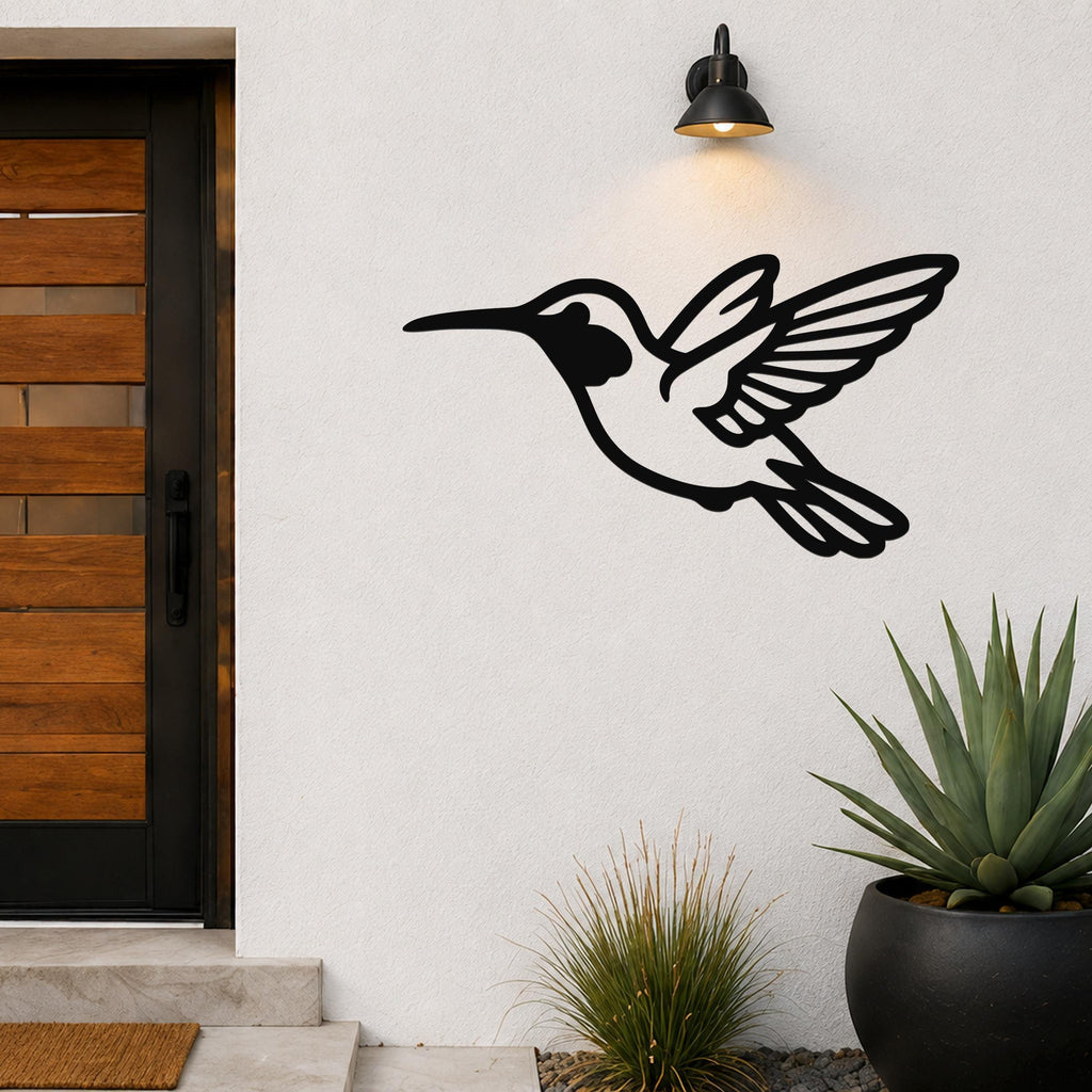Black metal hummingbird wall art with wing and tail cutouts, mounted on a white exterior wall above a potted succulent near a front door.