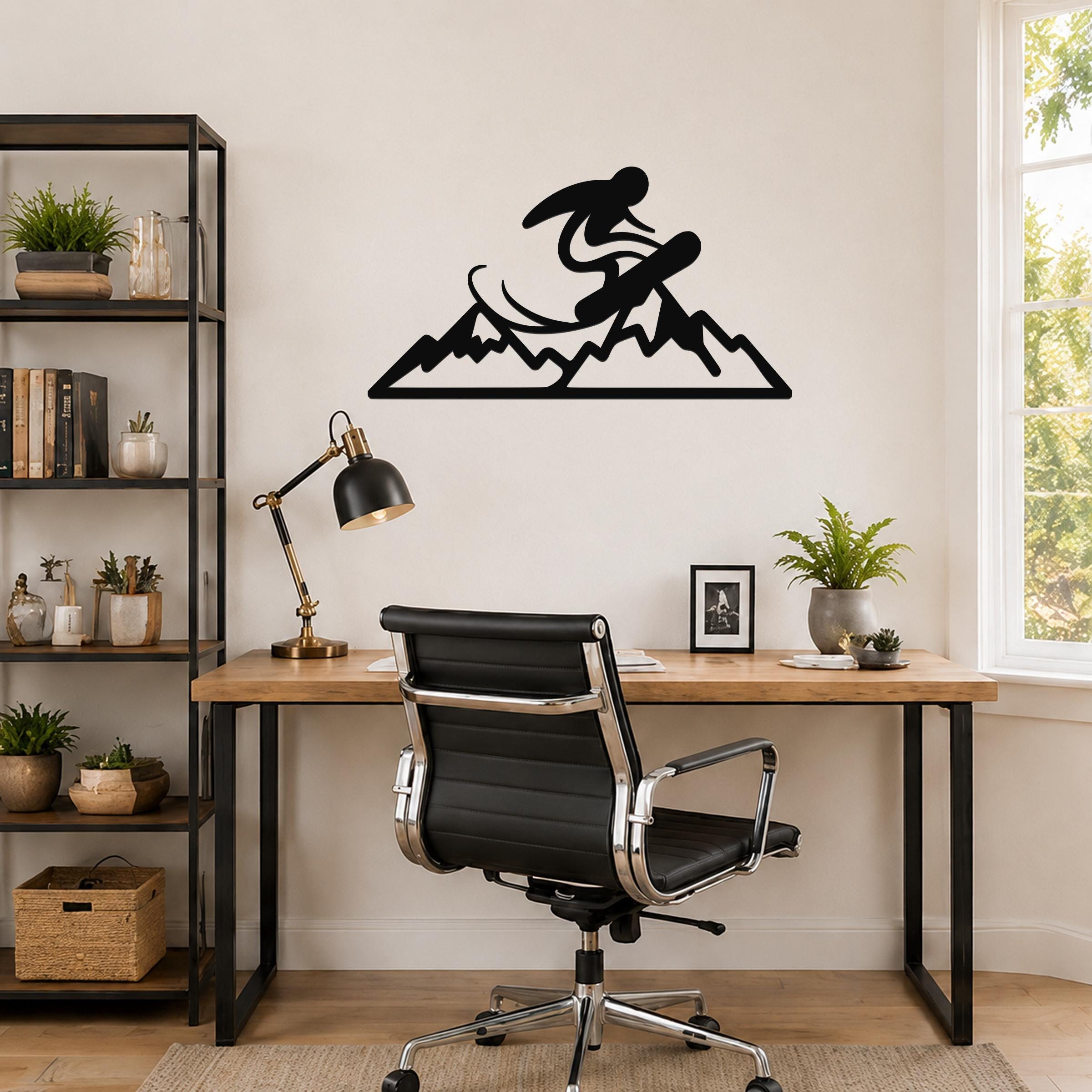 Black metal wall art featuring a snowboarder silhouette above a mountain range, mounted on a wall above a wooden desk in a home office.
