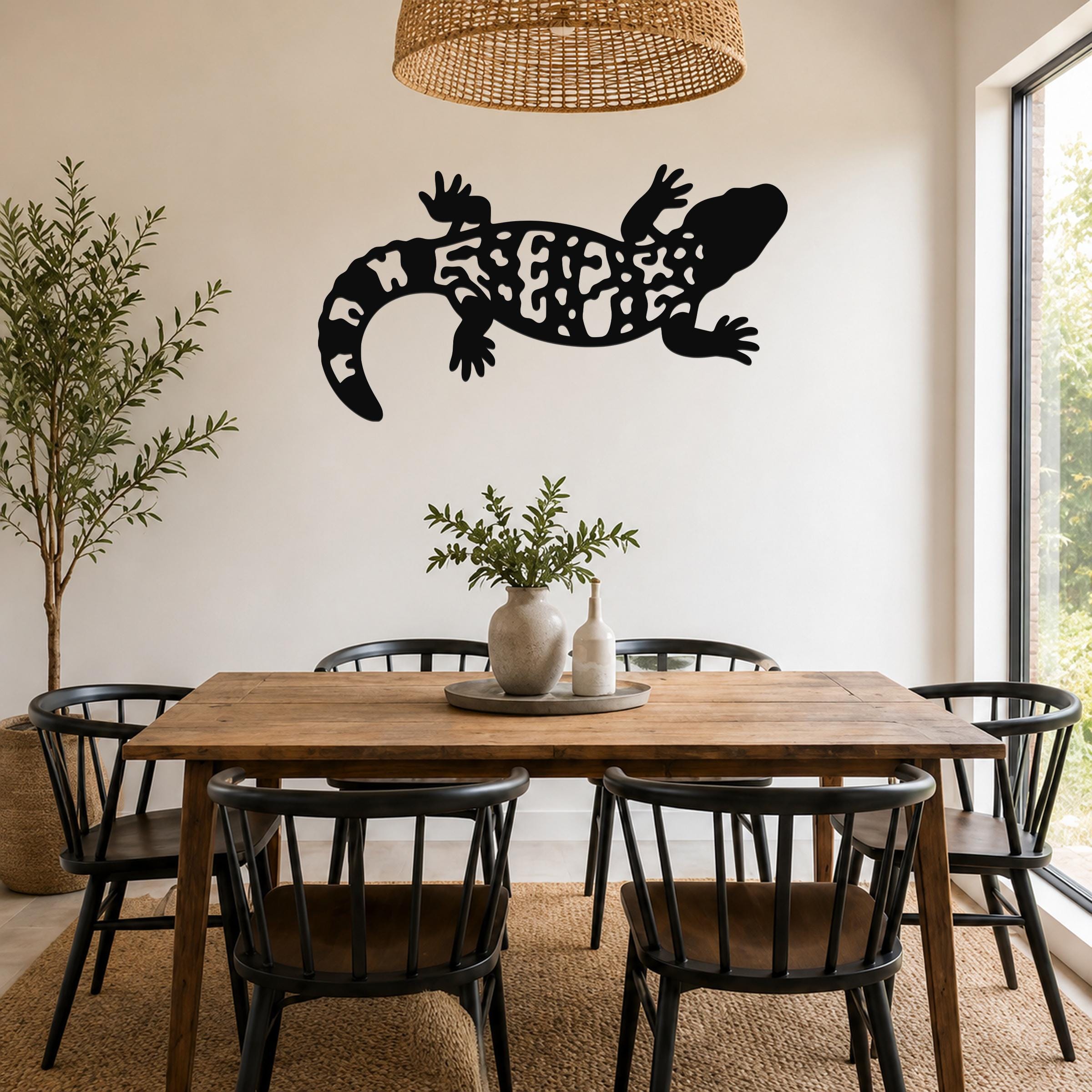 Black metal wall art of a Gila monster with intricate cutout patterns, mounted on a wall above a wooden dining table in a bright, modern dining room.