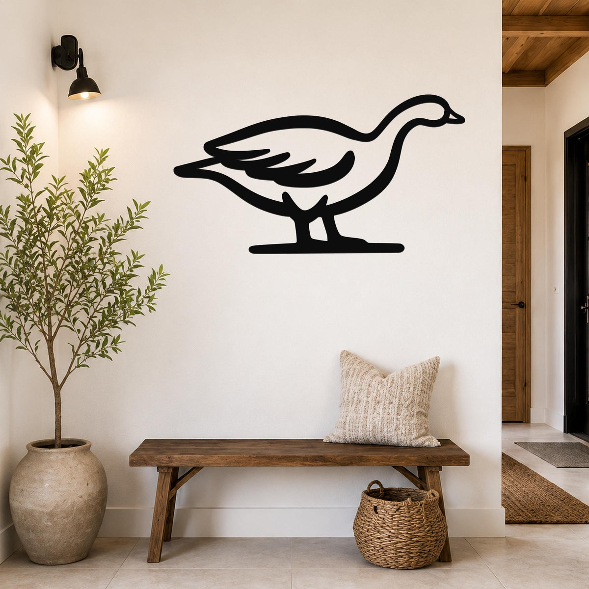 Black metal goose wall art silhouette mounted on a white wall above a wooden bench in a hallway.