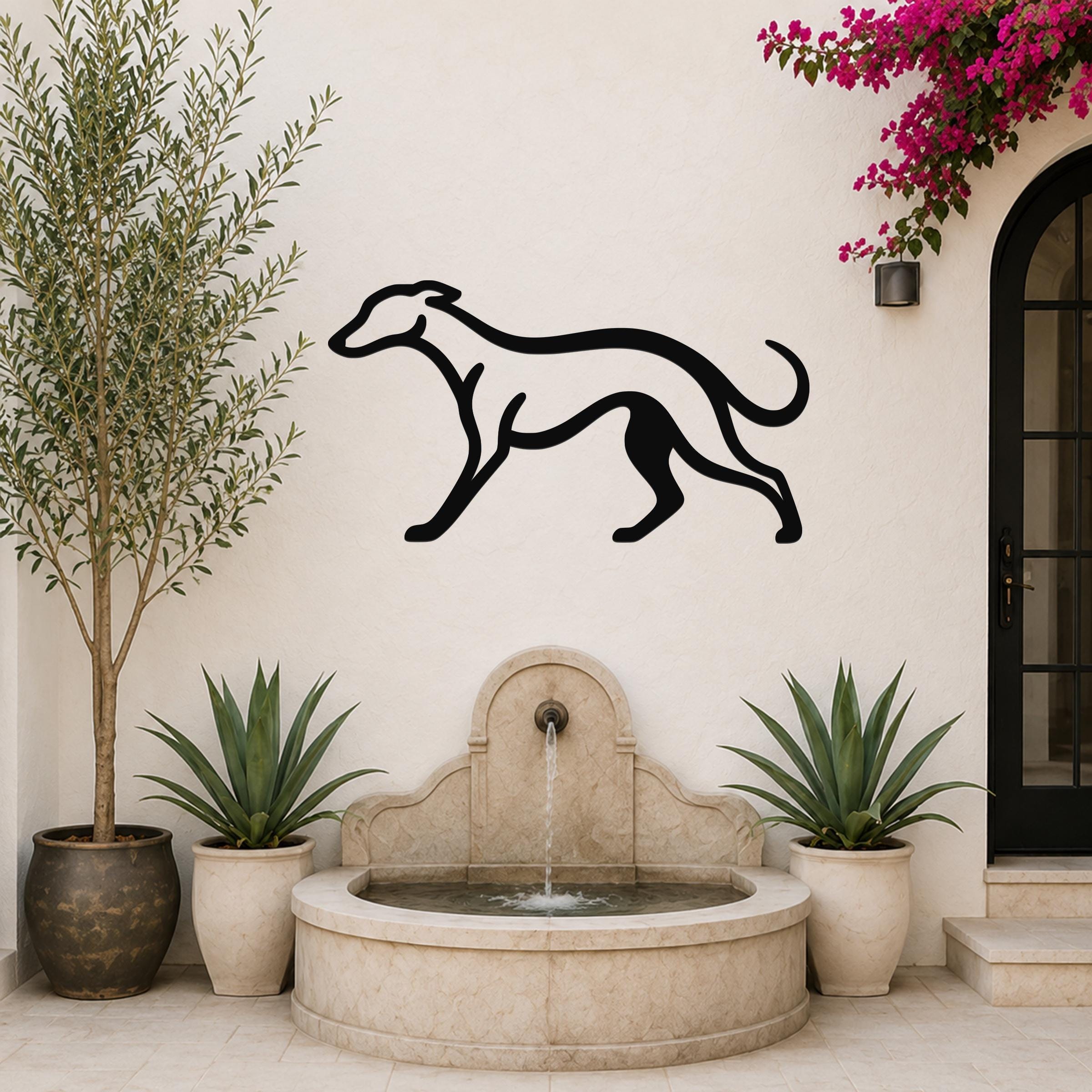 Black metal greyhound wall art silhouette mounted on a white outdoor wall above a stone fountain, flanked by potted plants and a flowering vine.