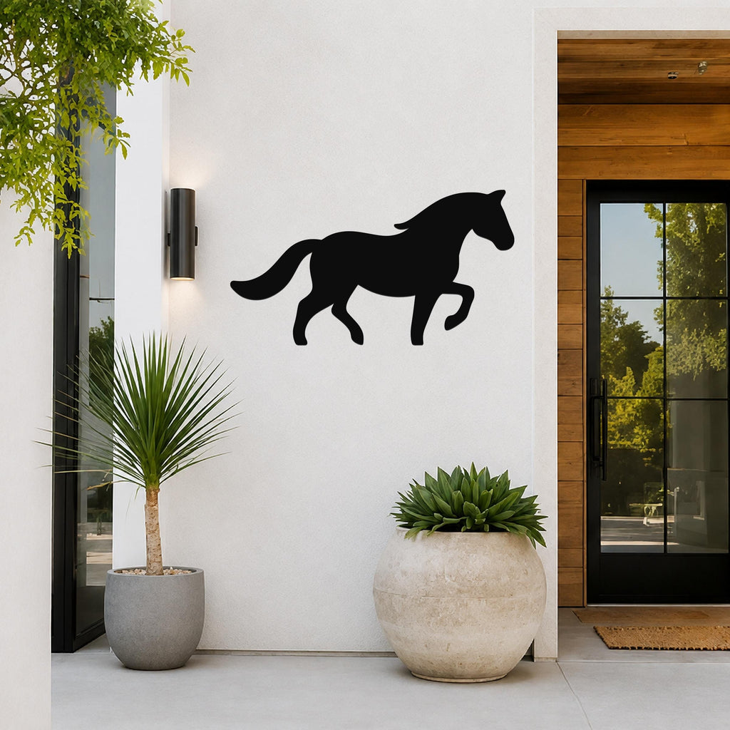 Black metal horse silhouette wall art mounted on a white exterior wall beside a glass door and potted plants.