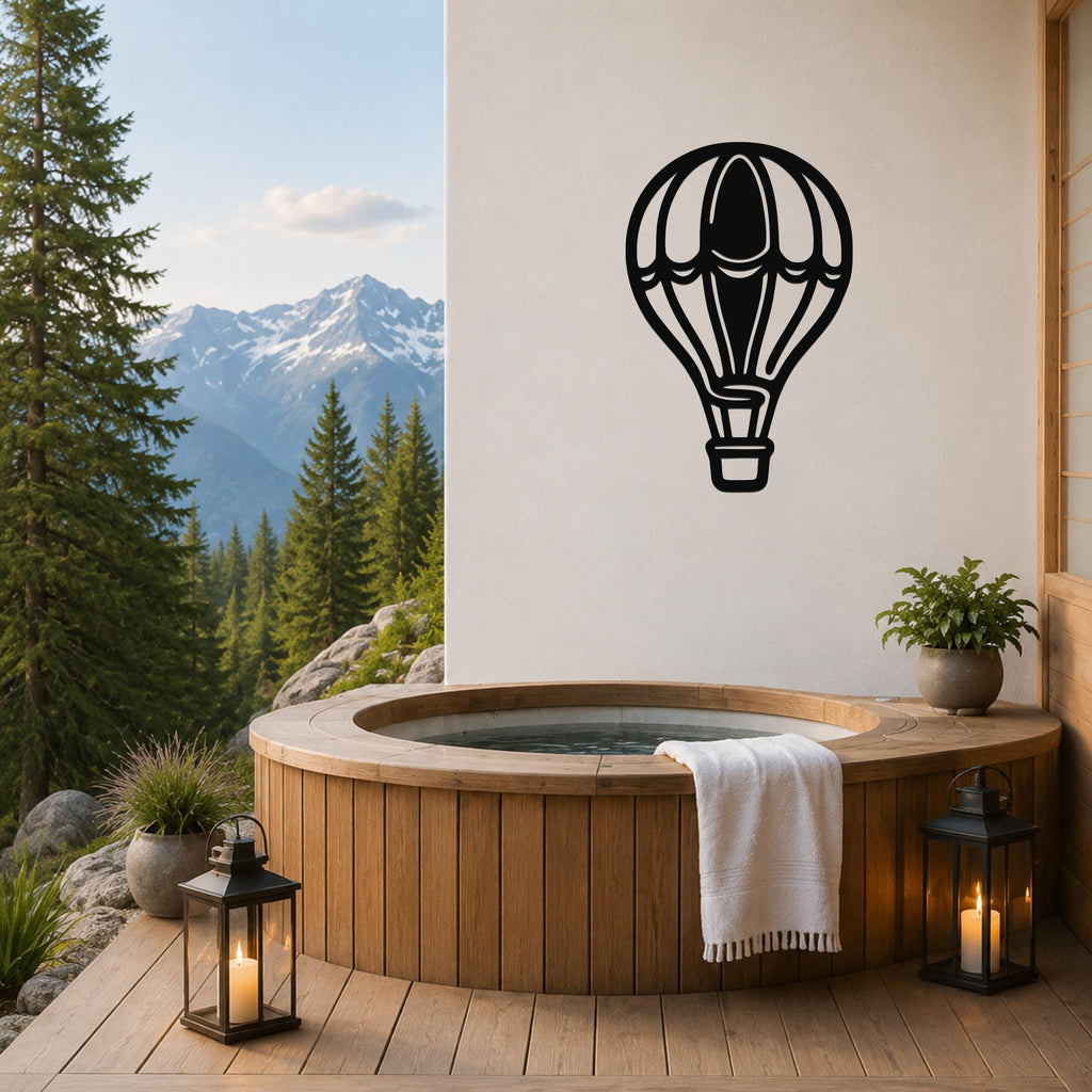 Black metal hot air balloon wall art with internal cutout details, mounted on a white wall above a wooden hot tub on a mountain-view deck.