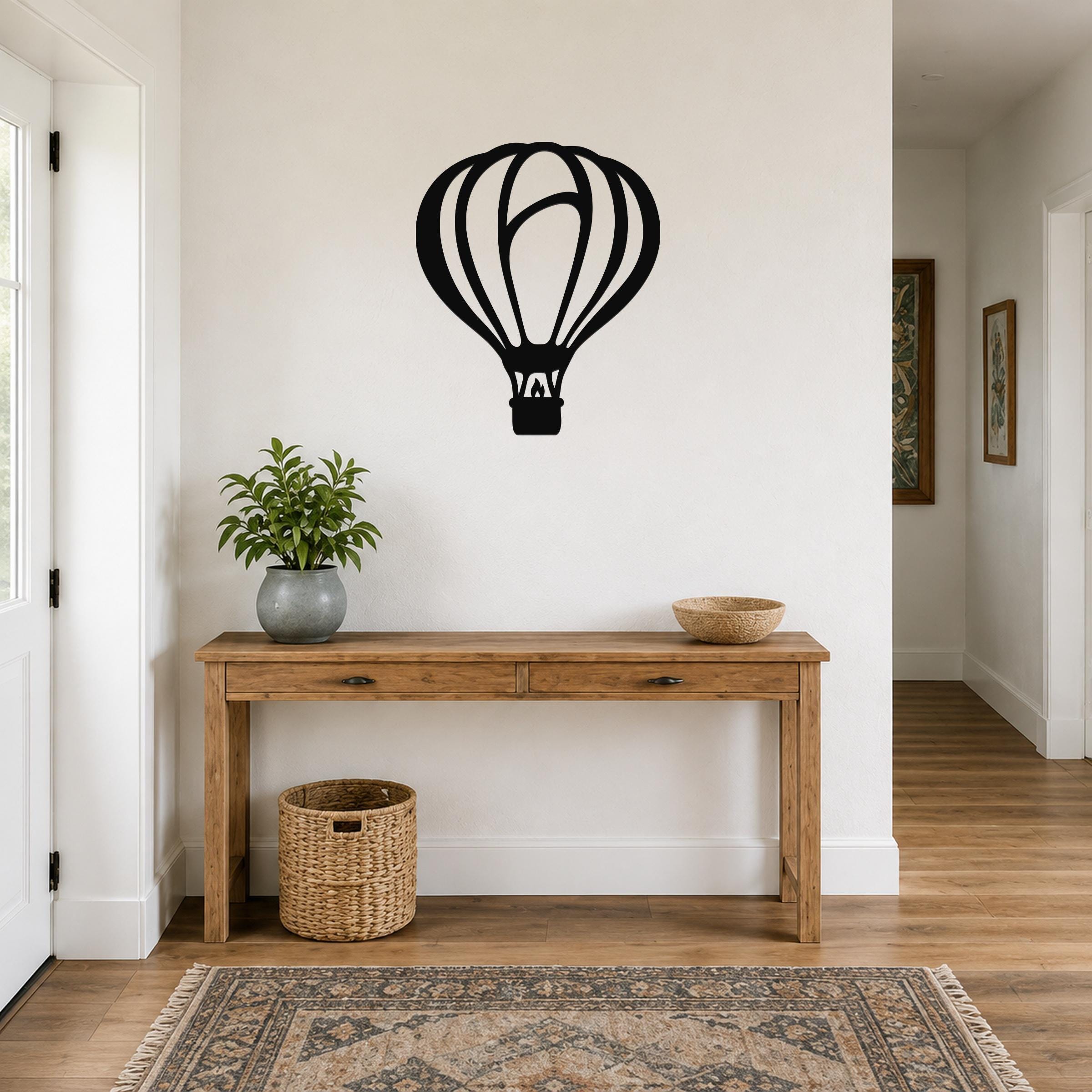 Black metal hot air balloon wall art with internal cutout lines, mounted on a white wall above a wooden console table in a hallway.