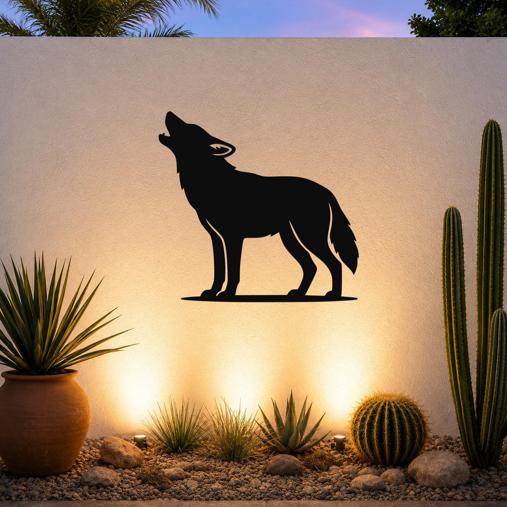 Black metal coyote wall art in a howling silhouette, mounted on an outdoor wall above a desert garden with cacti and warm uplighting.