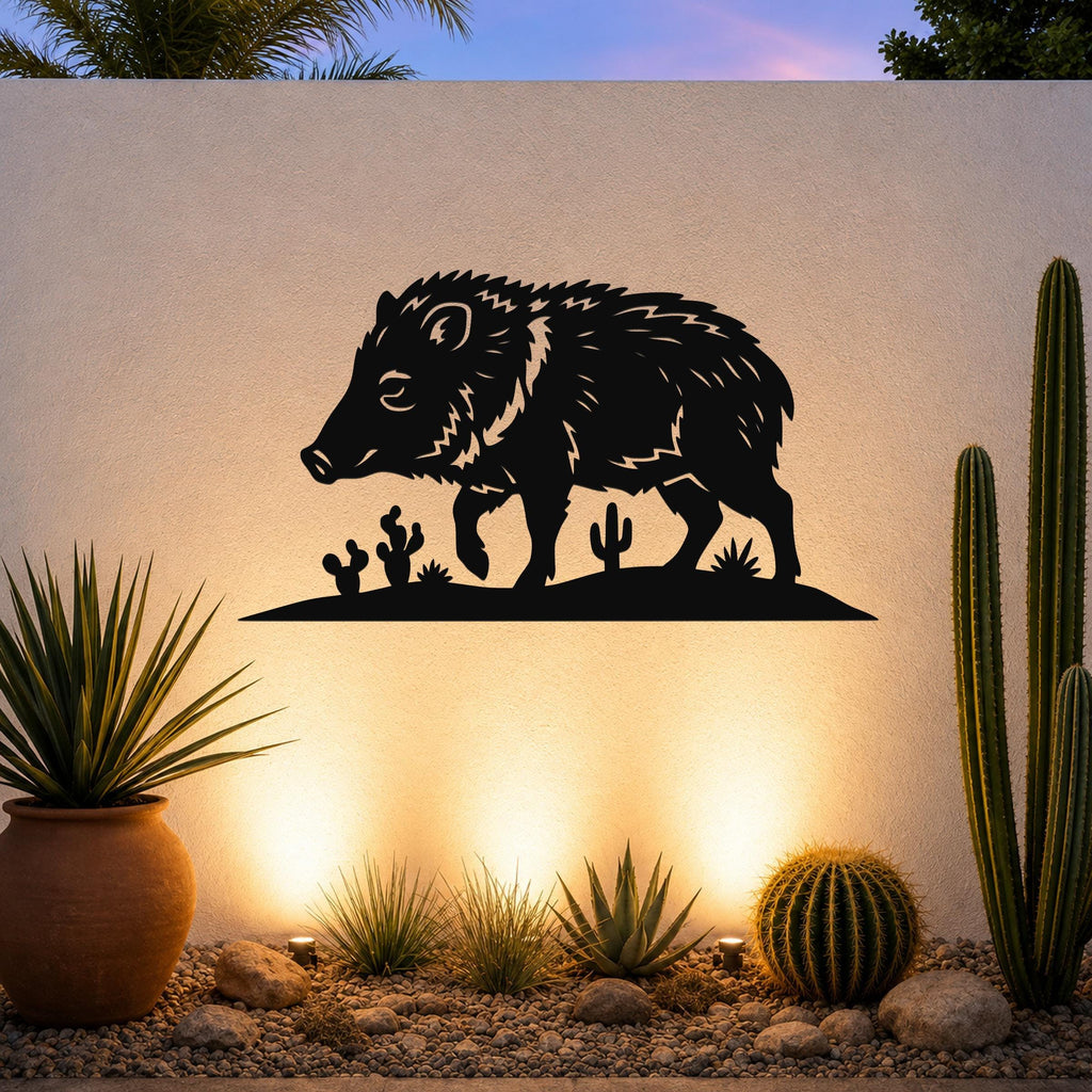 Black metal javelina wall art with cactus cutouts, mounted on an outdoor wall above a desert garden with potted plants and ground lights.