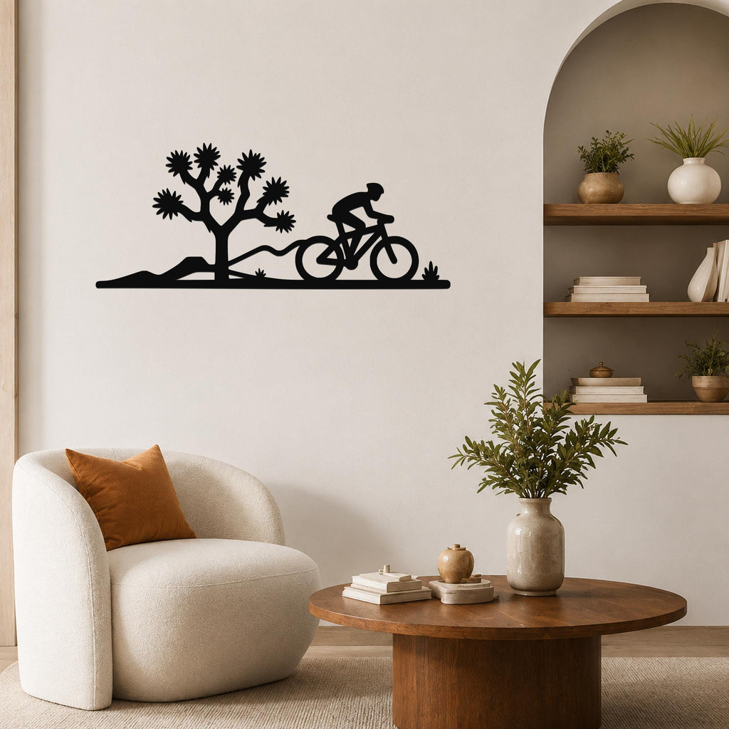 Black metal wall art silhouette of a cyclist and Joshua tree, mounted on a living room wall above a white armchair.