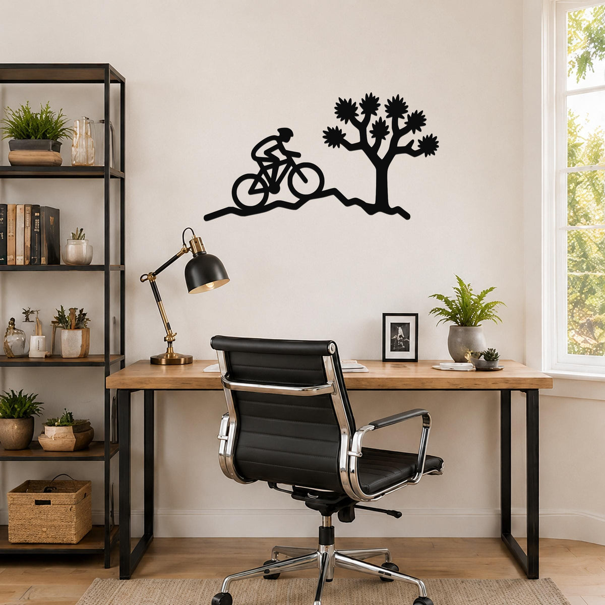 Black metal wall art cutout of a cyclist and a Joshua tree, mounted above a wooden desk in a home office.