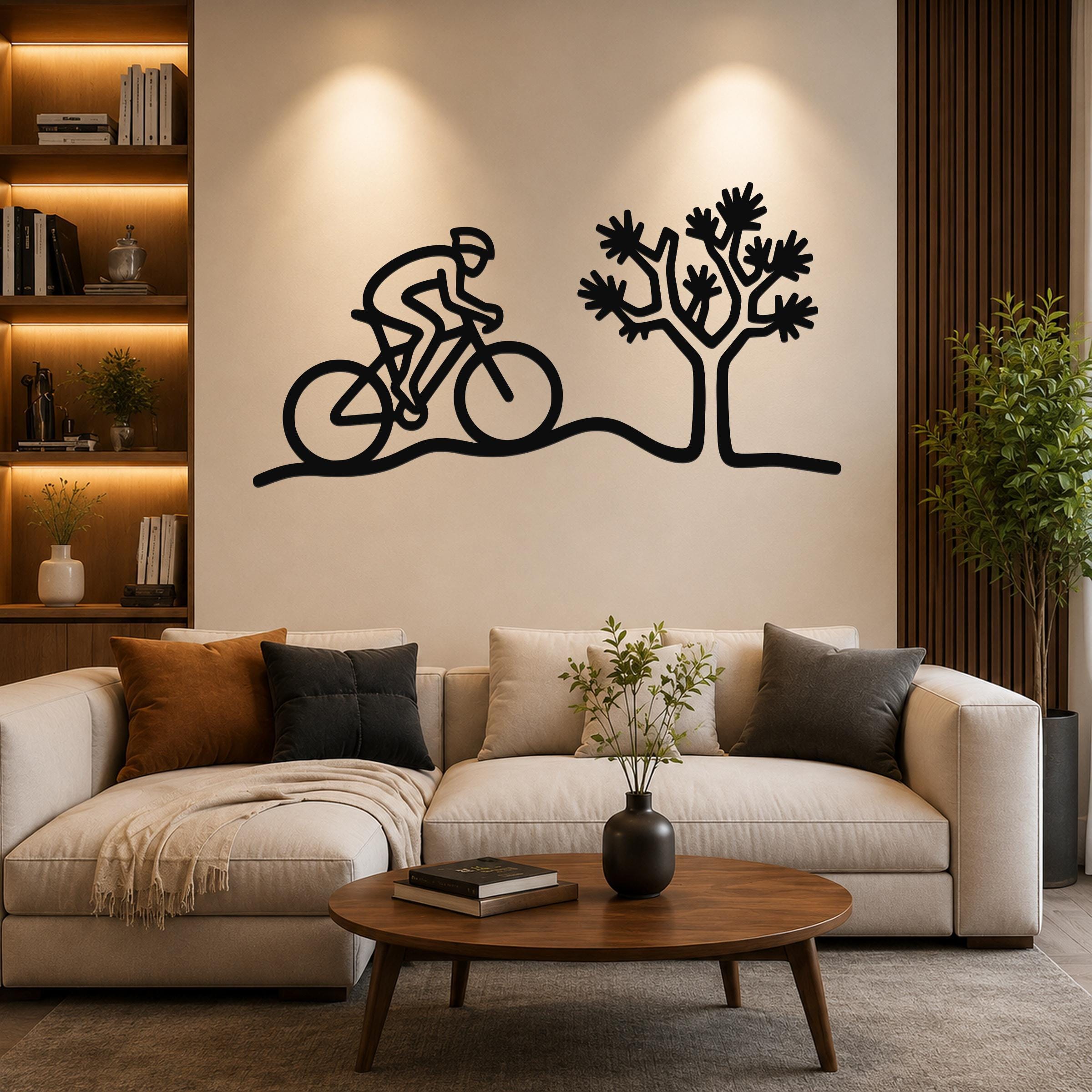 Black metal wall art silhouette of a cyclist on a desert trail with a Joshua tree, mounted above a sofa in a living room.