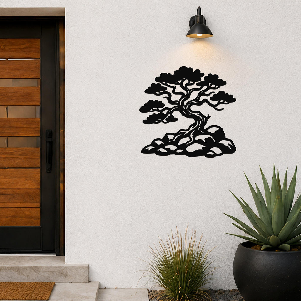 Black metal wall art silhouette of a juniper tree with rocky base, mounted on an outdoor wall beside a wooden door and potted plants.