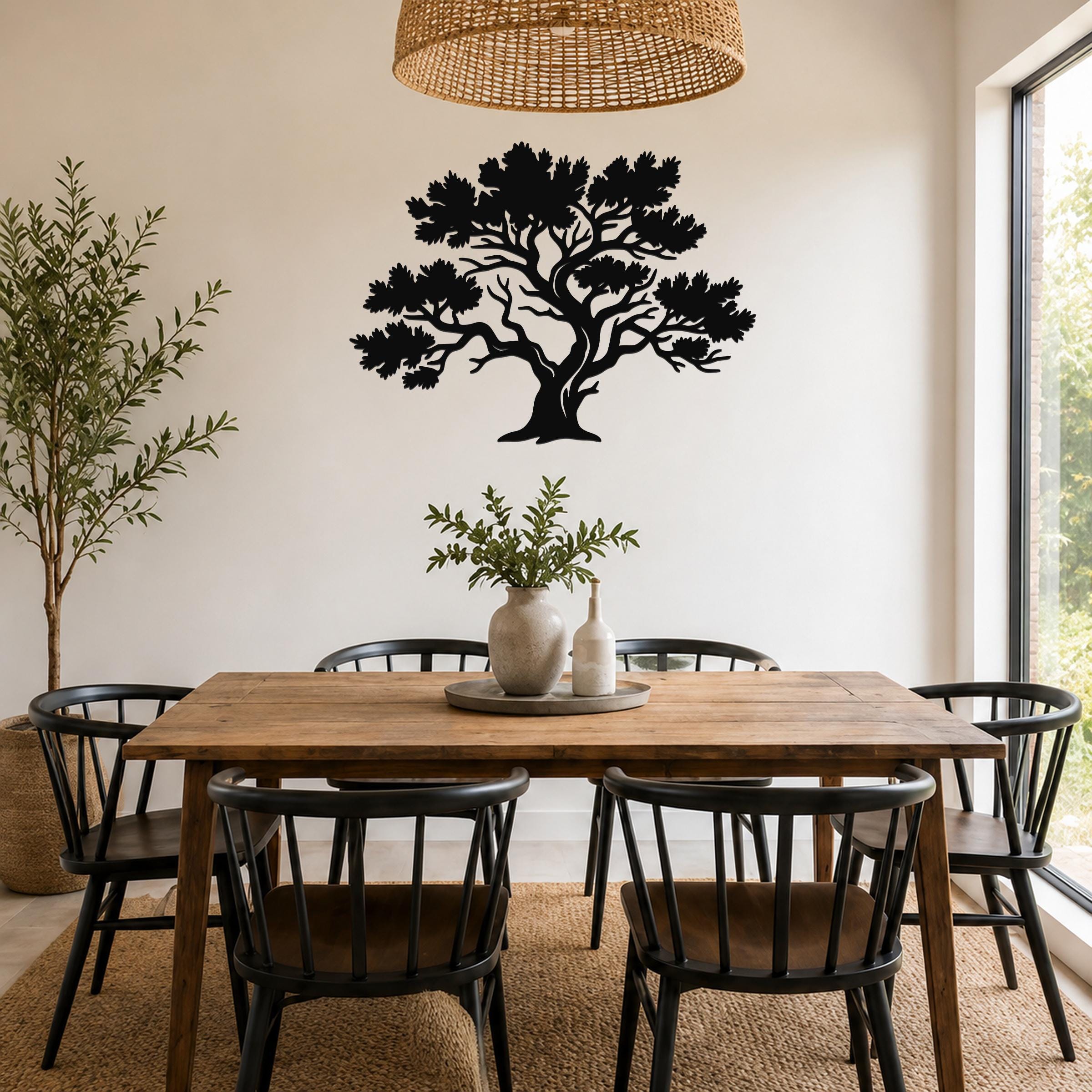 Black metal juniper tree wall art with detailed branch cutouts, mounted on a white wall above a wooden dining table in a bright dining room.