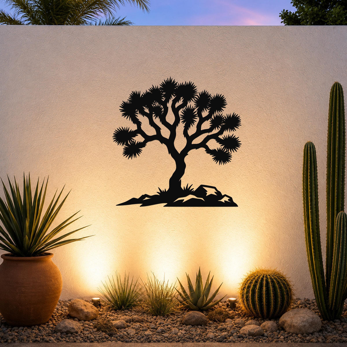 Black metal wall art silhouette of a Joshua tree with spiky branches and rocky base, mounted on an outdoor wall above a desert garden with cacti and warm uplighting.