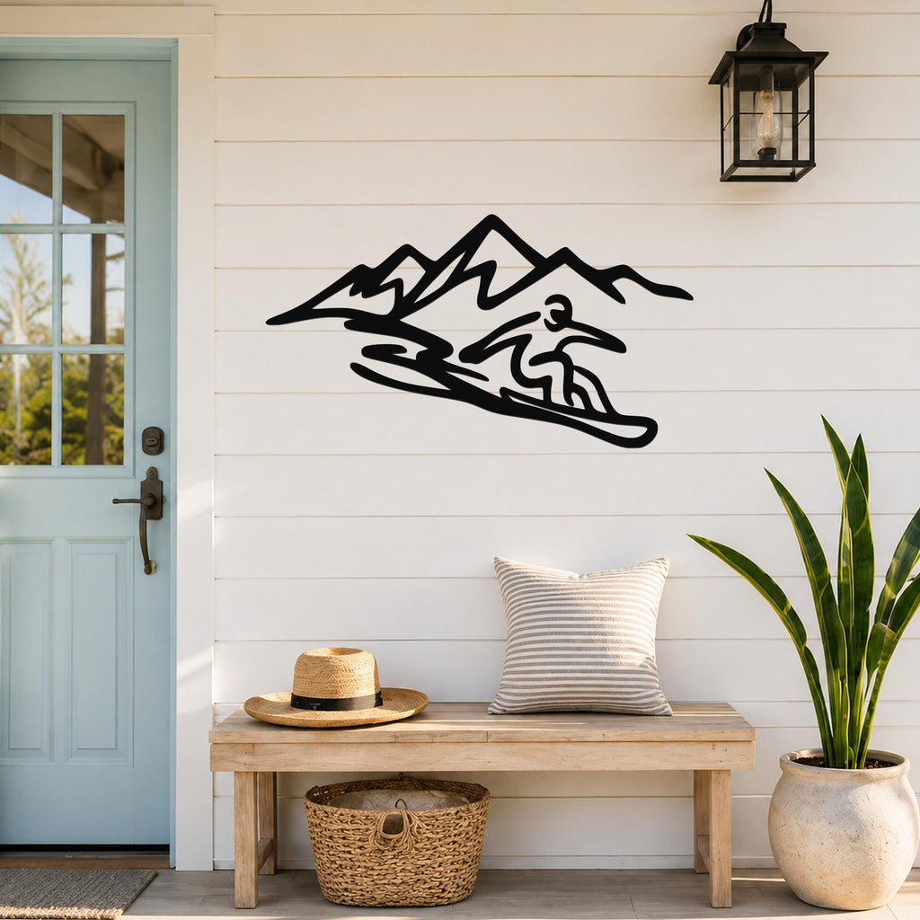 Black metal wall art silhouette of a snowboarder in motion with mountain peaks, mounted on a white shiplap wall above a wooden bench in a porch entryway.