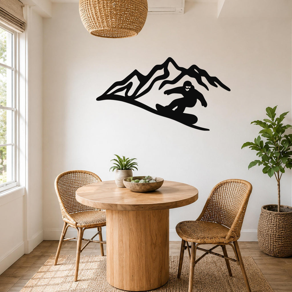 Black metal wall art silhouette of a snowboarder on a mountain slope, mounted on a white wall above a round wooden table in a bright dining area.