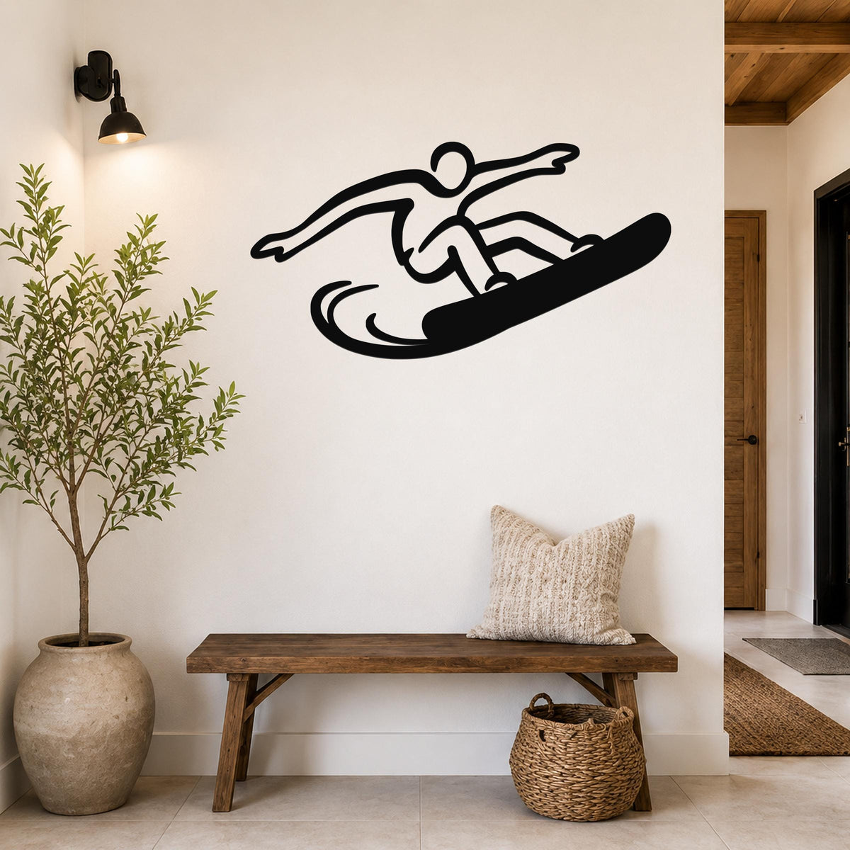 Black metal snowboarder wall art with a dynamic silhouette cutout, mounted on a white wall above a wooden bench in a modern entryway.