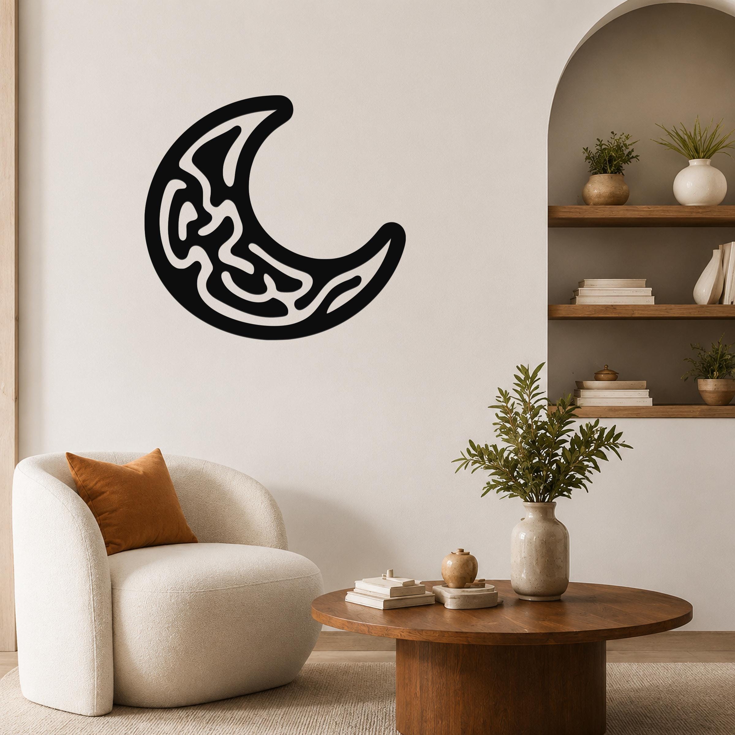 Black metal crescent moon wall art with intricate internal cutouts, mounted on a living room wall above a white armchair.
