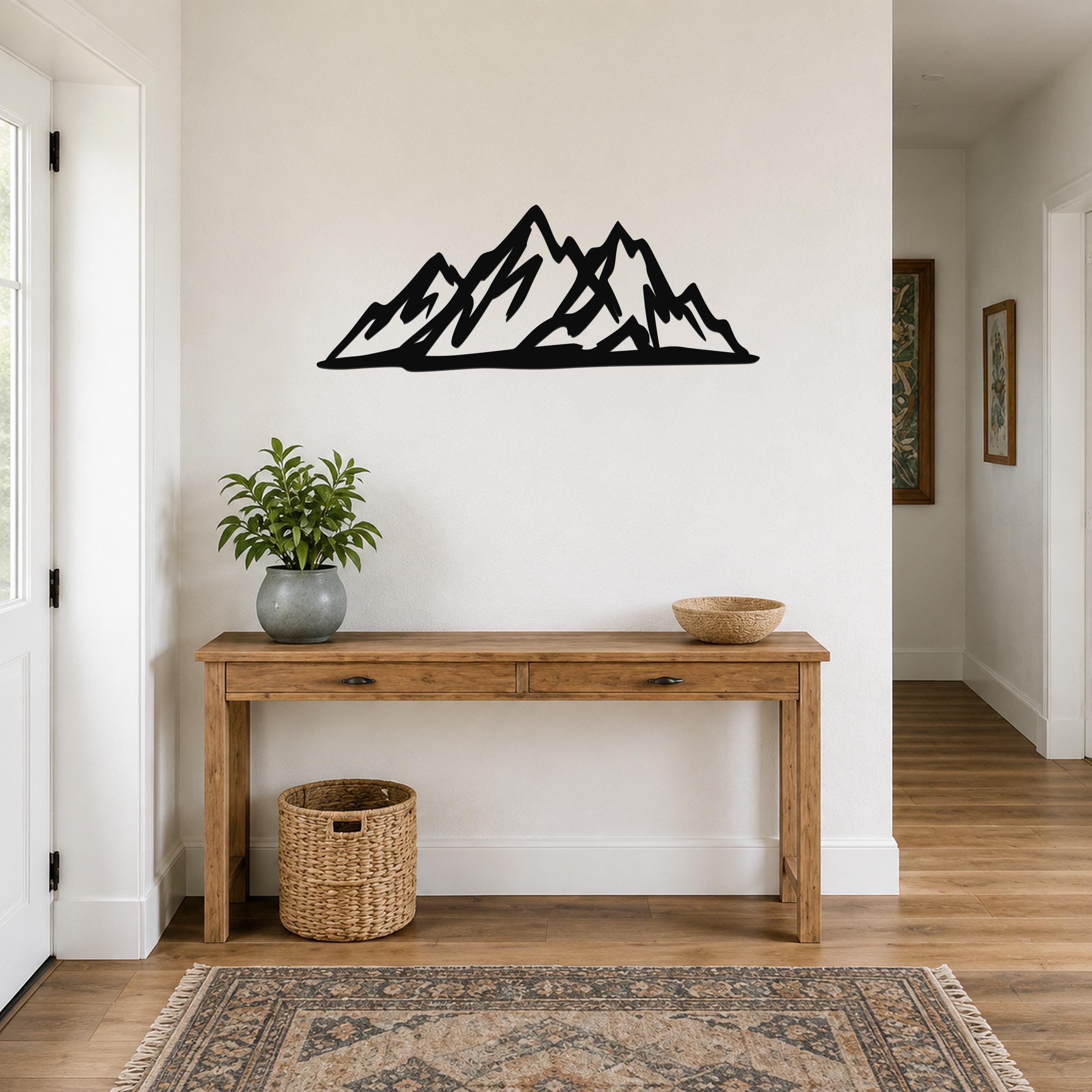 Black metal mountain silhouette wall art with layered peaks, mounted above a wooden console table in a hallway.