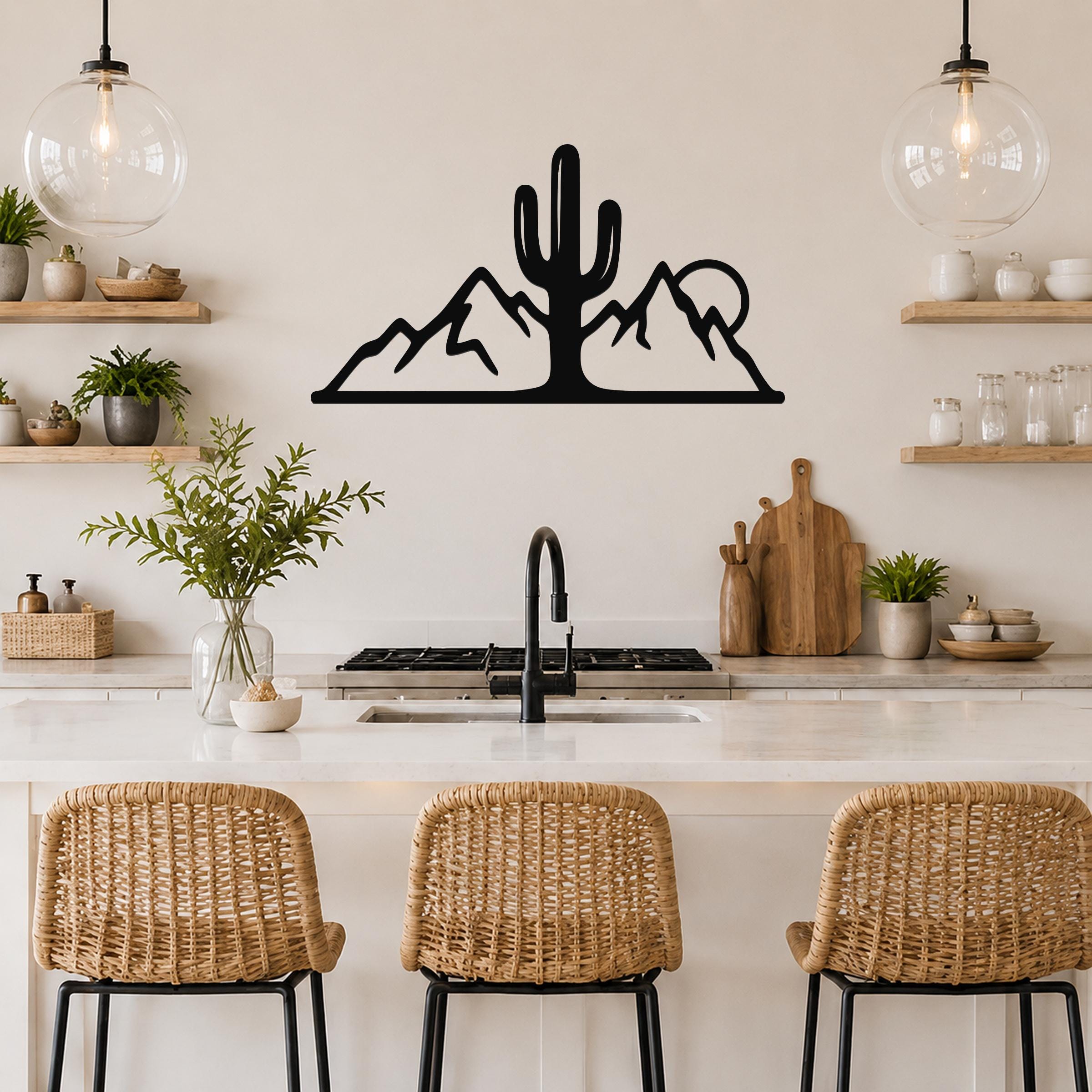 Black metal wall art silhouette of a saguaro cactus and mountain range, mounted above a kitchen counter with open shelving and pendant lights.