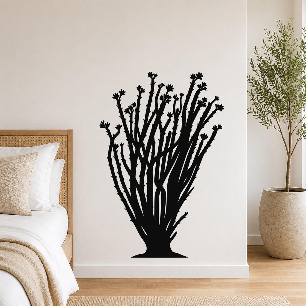 Black metal ocotillo wall art with branching stems and flower cutouts, mounted on a bedroom wall above a bed.
