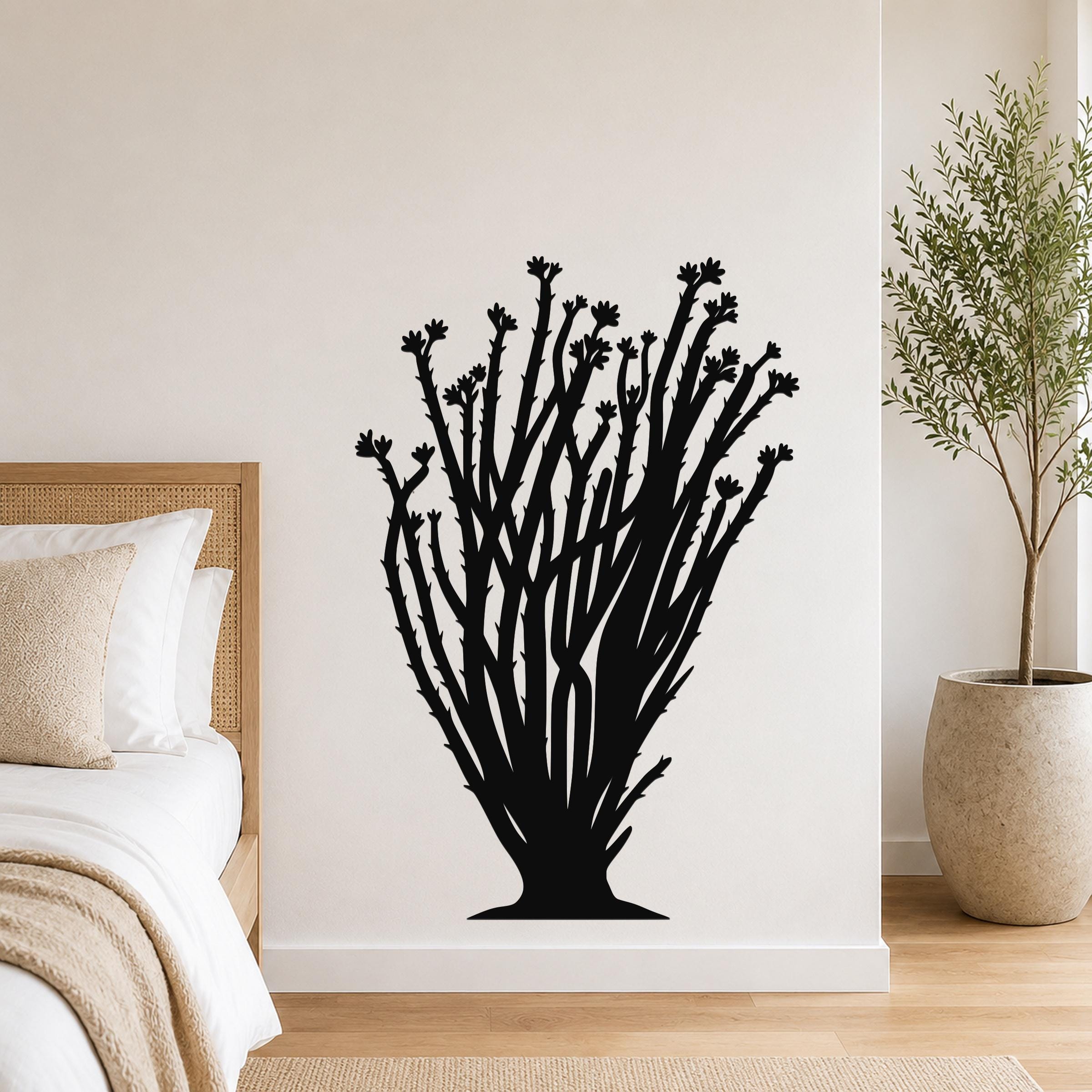 Black metal ocotillo wall art with branching stems and flower cutouts, mounted on a bedroom wall above a bed.
