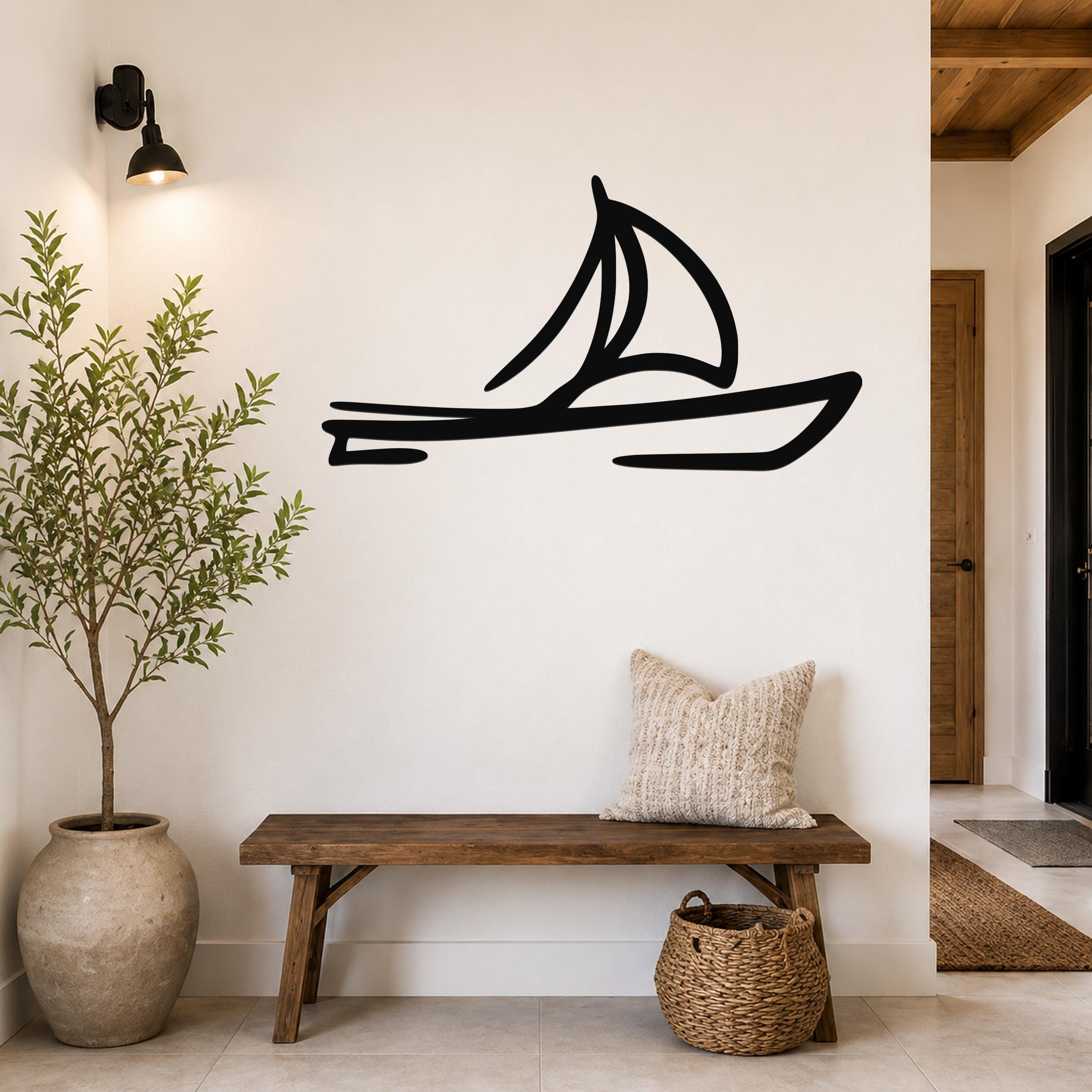Black metal sailboat wall art silhouette mounted on a white wall above a wooden bench in a coastal entryway.