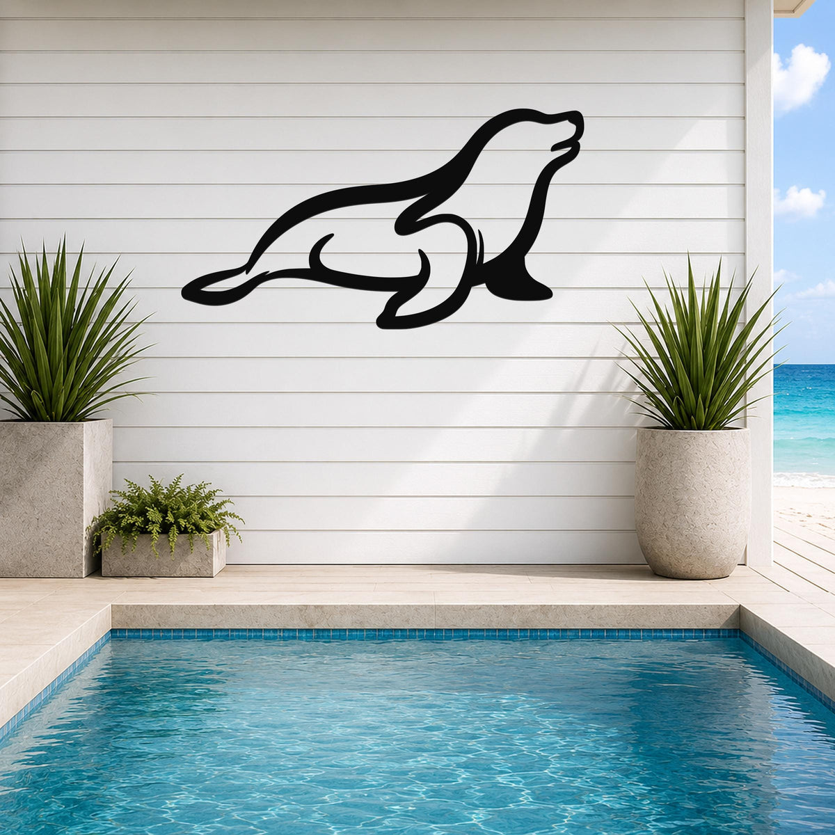 Black metal sea lion wall art with a sleek silhouette design, mounted on a white shiplap wall above a pool with potted plants and ocean views.