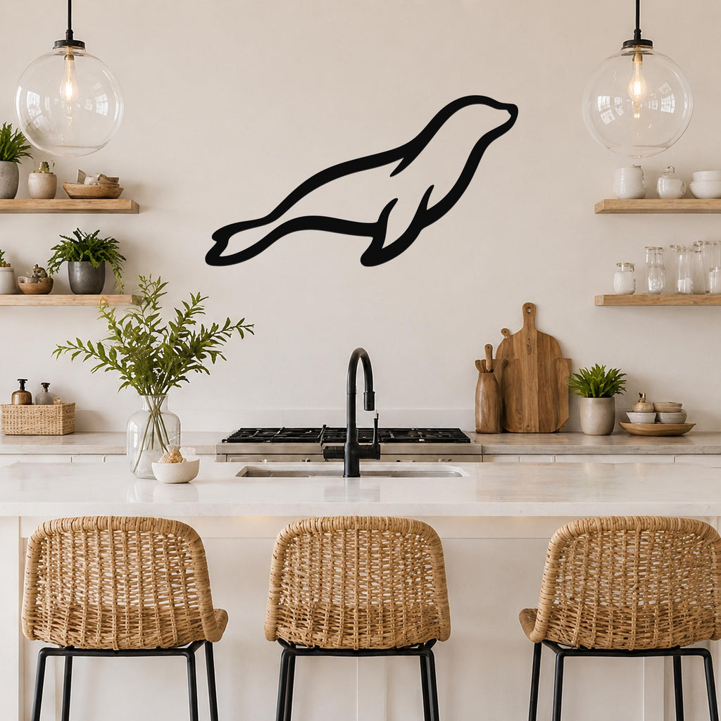 Black metal sea lion wall art silhouette mounted above a kitchen counter, displayed in a modern kitchen with wooden shelves and pendant lights.