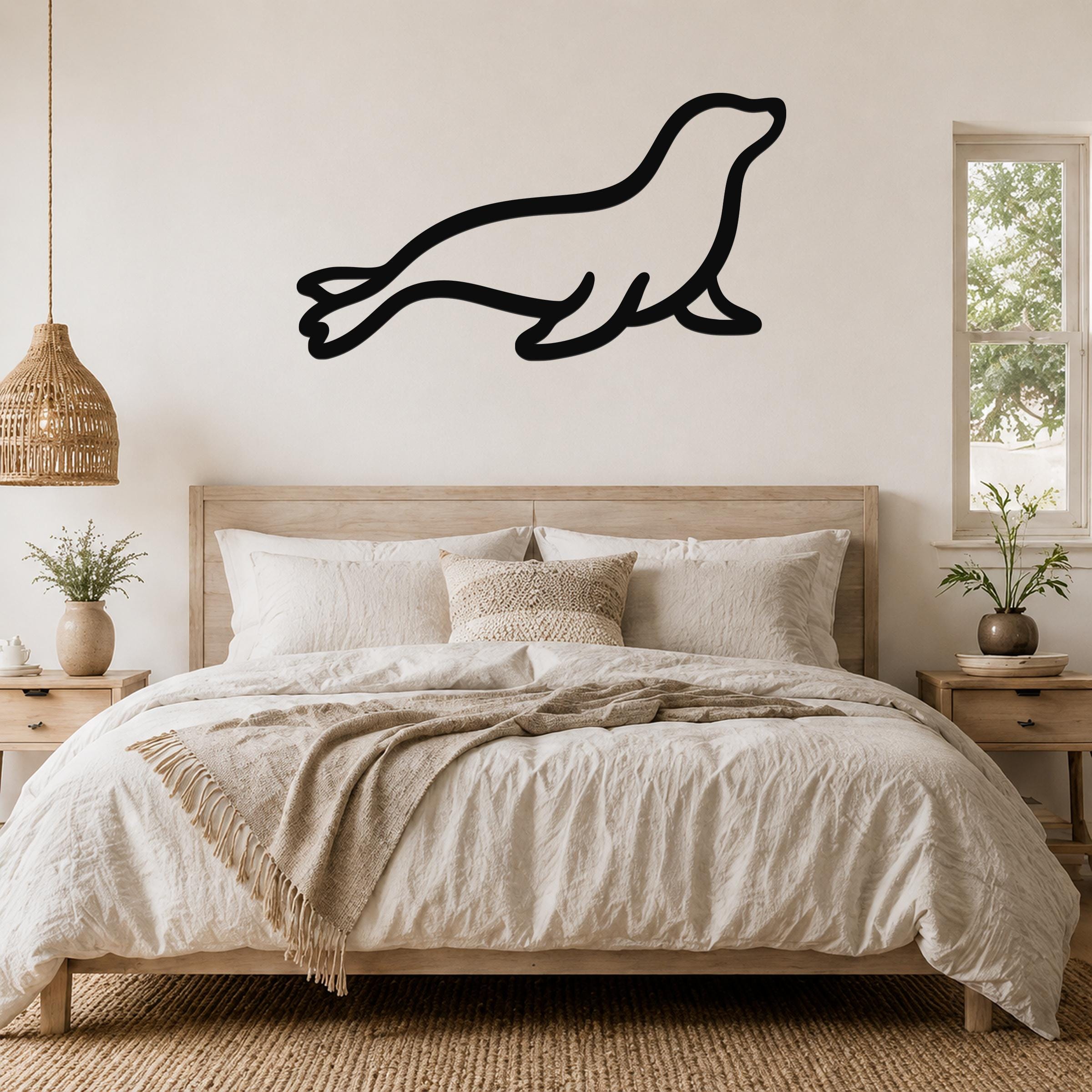 Black metal sea lion wall art in a silhouette style, mounted above a wooden bed in a neutral bedroom.