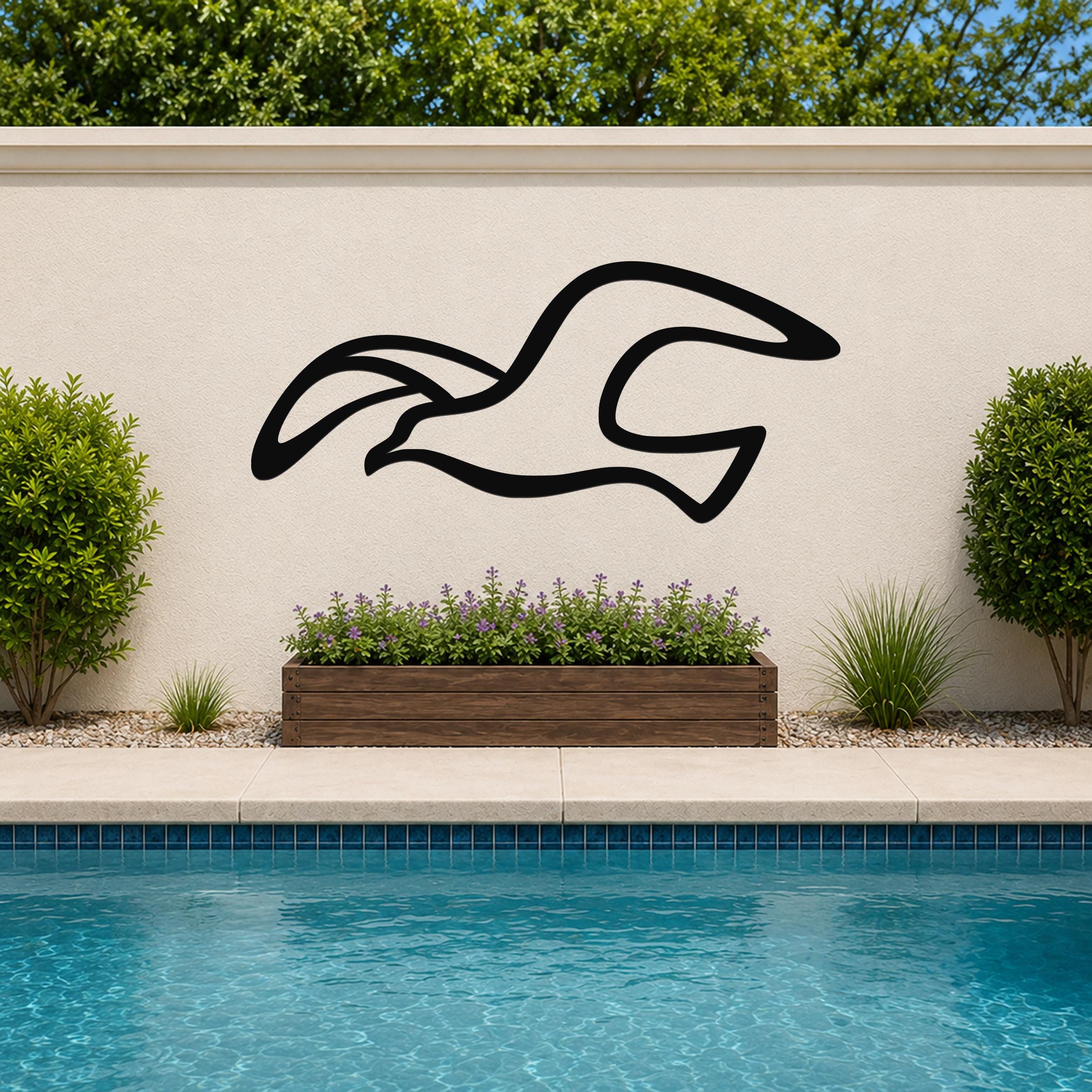 Black metal seagull wall art with flowing motion-line cutouts, mounted on an outdoor wall above a poolside planter.