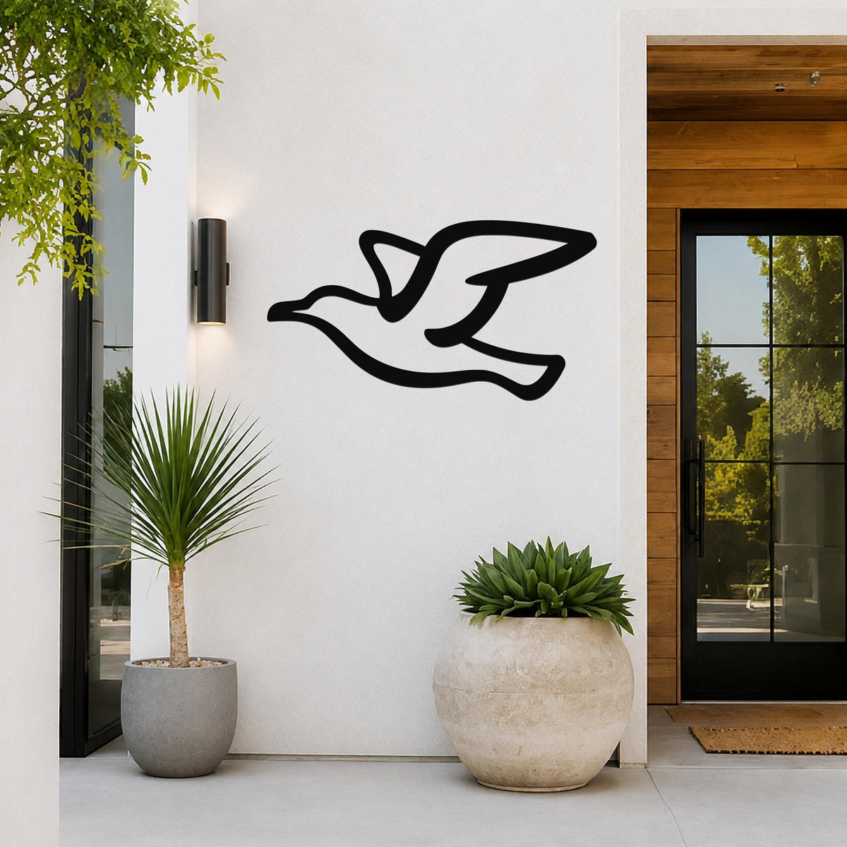 Black metal seagull wall art with a flowing silhouette, mounted on a white exterior wall beside a glass door and potted plants.