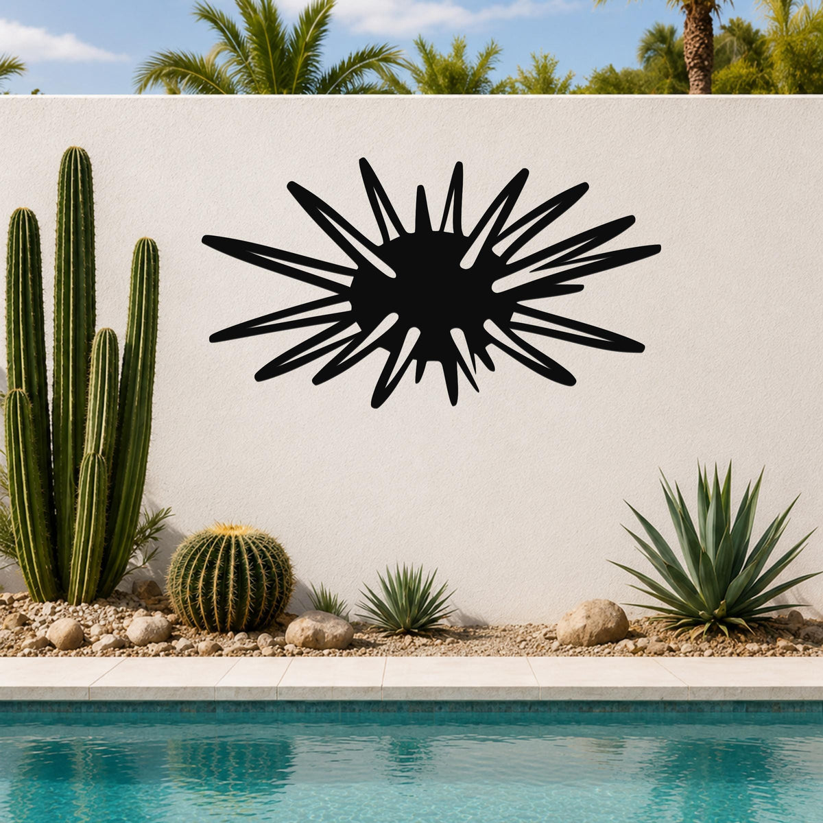 Black metal wall art in a sea urchin silhouette with radiating spines, mounted on an outdoor wall above a pool with cacti and palm trees in the background.