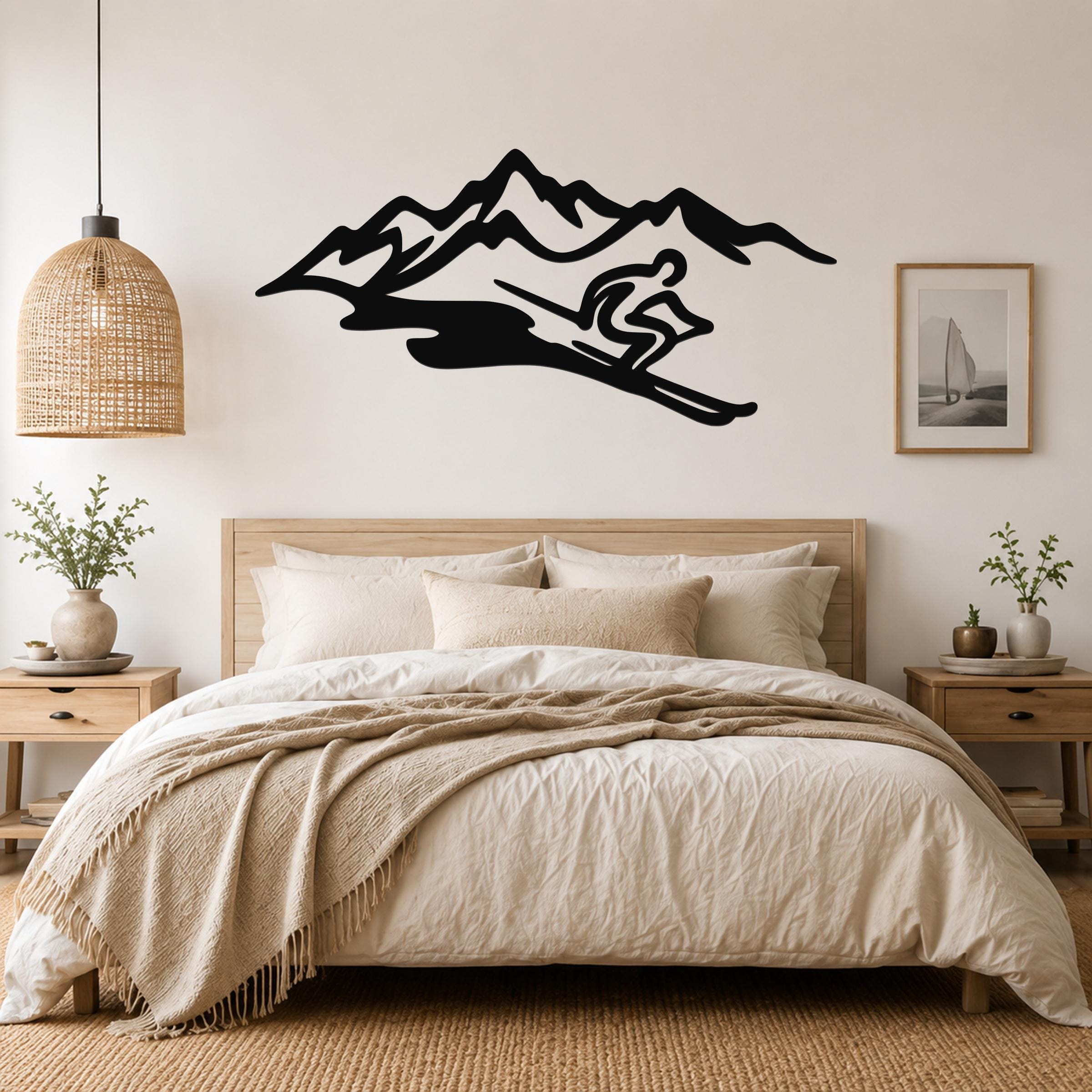 Black metal wall art featuring a skier silhouette descending a mountain range, mounted above a bed in a neutral bedroom.
