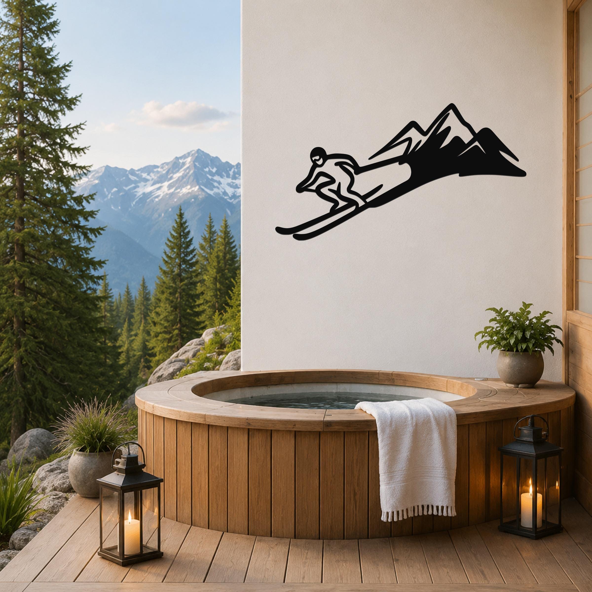 Black metal skier and mountain wall art silhouette mounted on a white wall above a wooden hot tub on a deck with a mountain view.