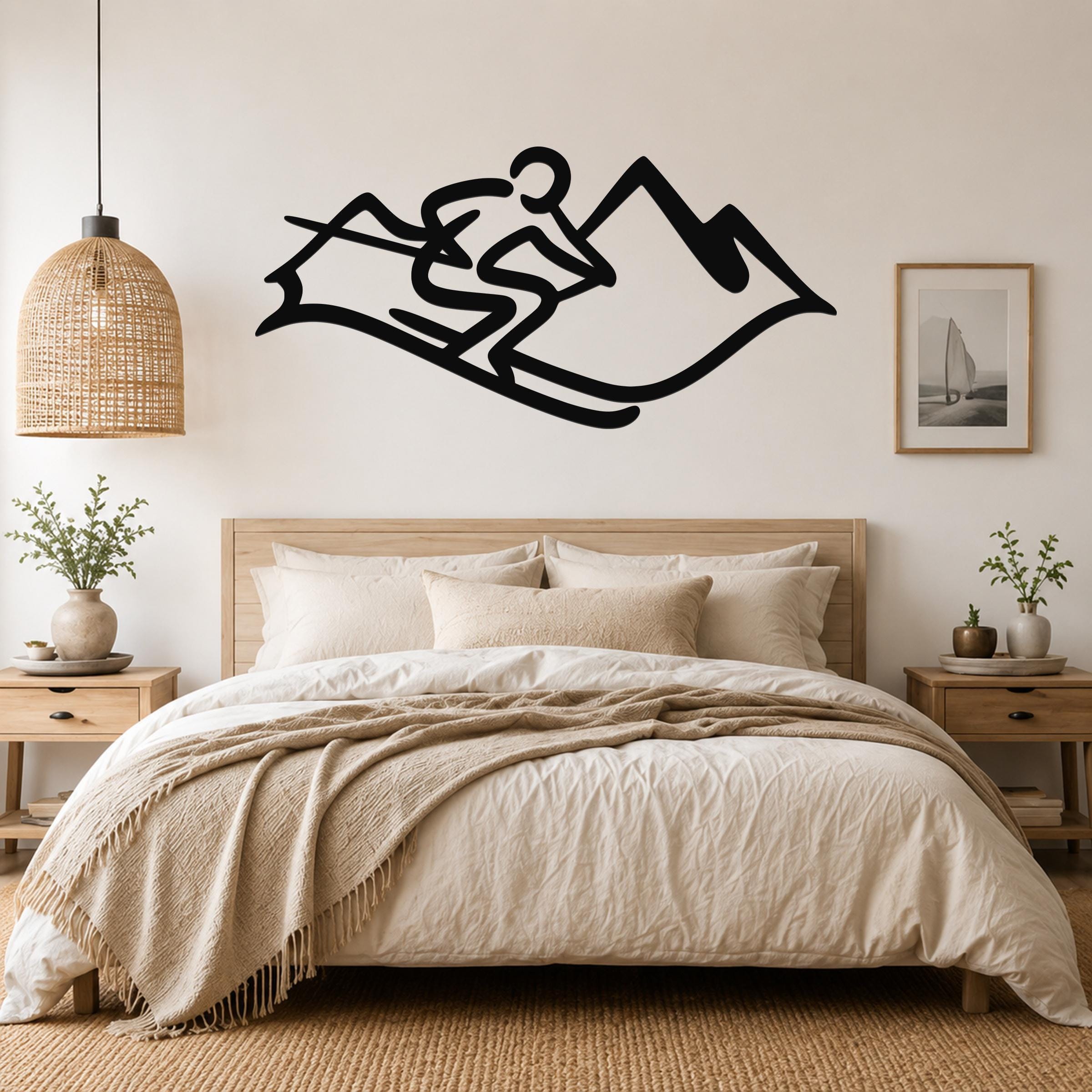 Black metal wall art silhouette of a skier in motion above a bed, mounted on a light-colored bedroom wall.