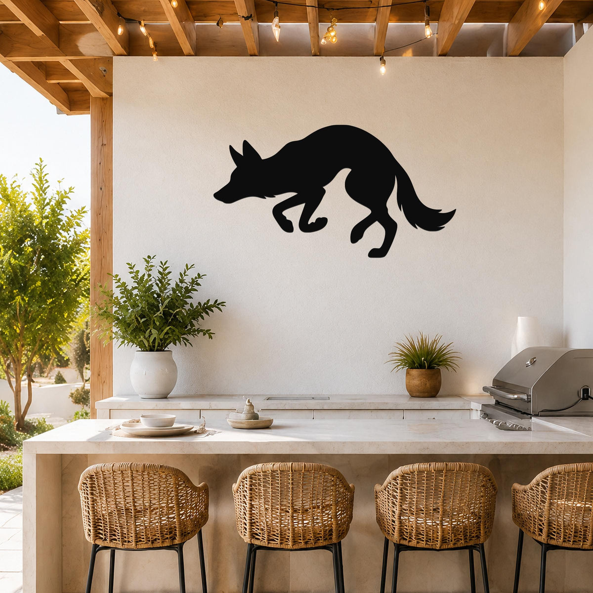Black metal coyote wall art silhouette mounted on a white outdoor kitchen wall above a counter with wicker bar stools.