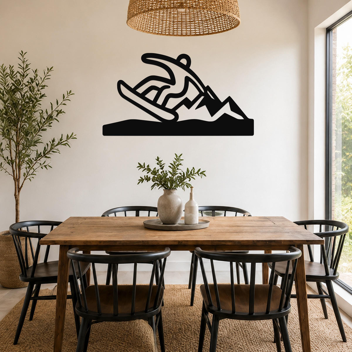Black metal wall sculpture of a snowboarder in motion, mounted above a wooden dining table in a bright room.