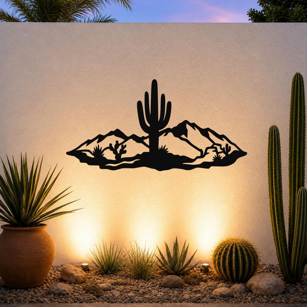 Black metal wall art silhouette of a desert scene with a saguaro cactus and mountains, mounted on an outdoor wall above a gravel garden with cacti and warm uplighting.