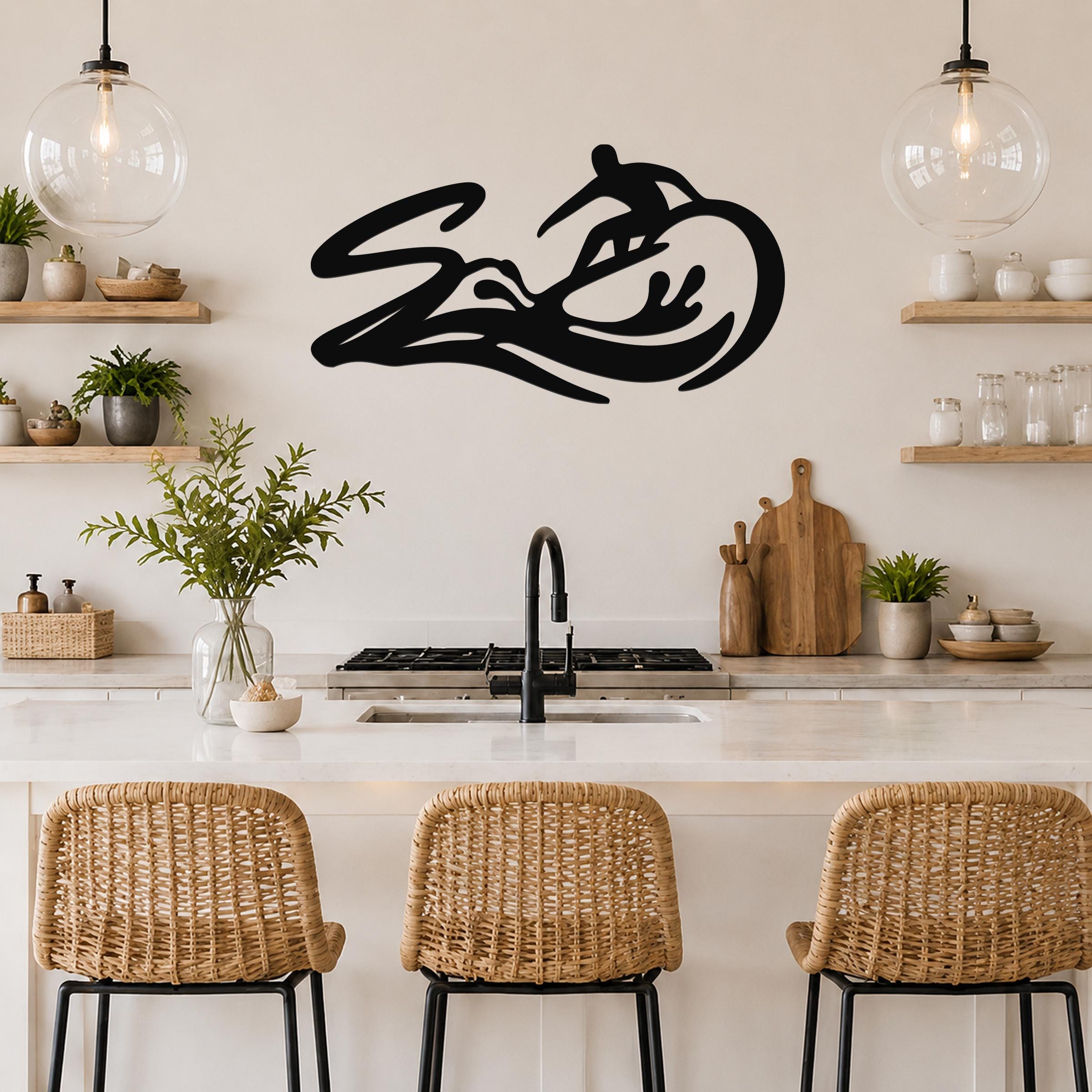 Black metal surfer wall art with wave and rider silhouette, mounted above a kitchen counter in a coastal-style kitchen.