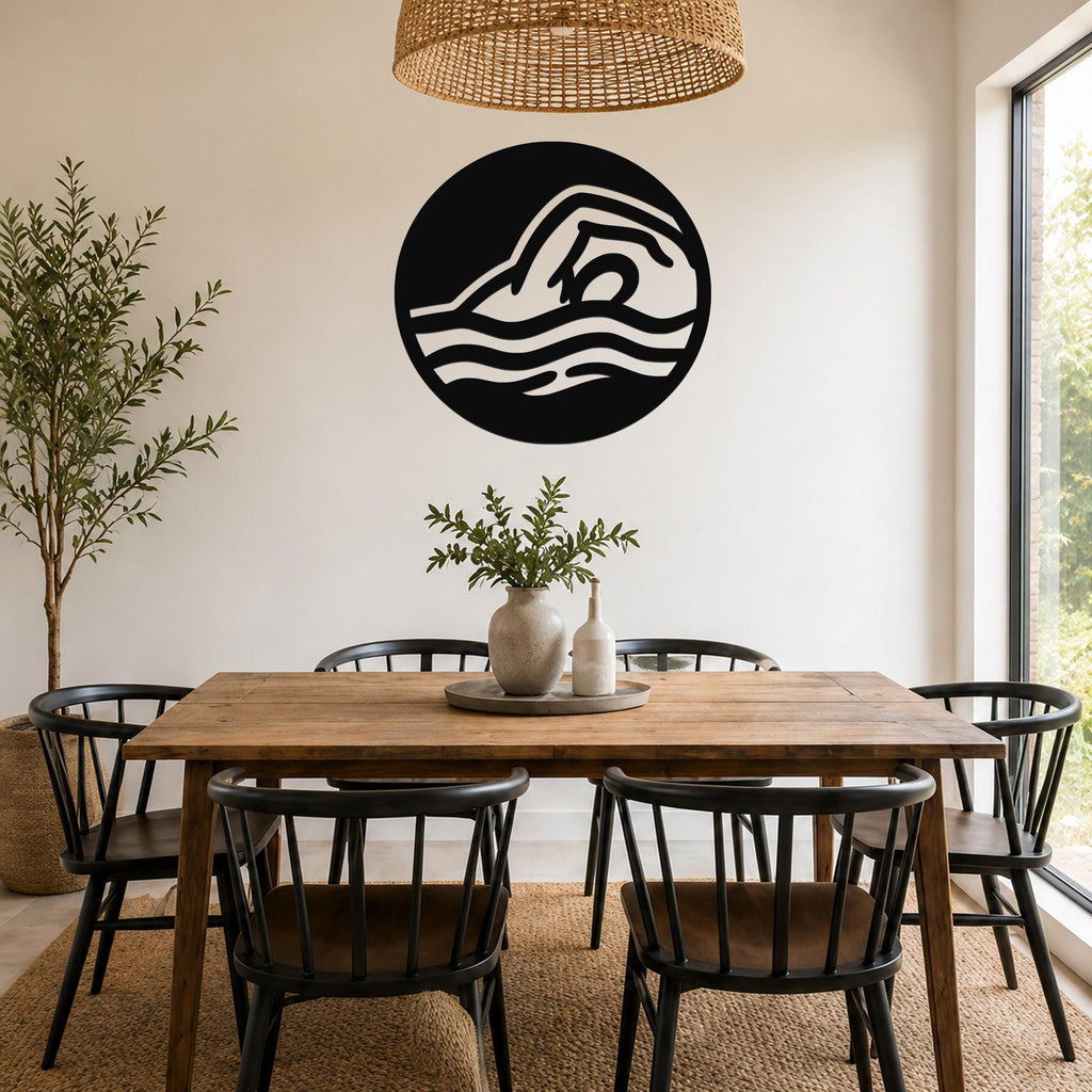 Black metal wall art with a swimmer silhouette in fluid motion, mounted on a white wall above a wooden dining table in a bright dining room.