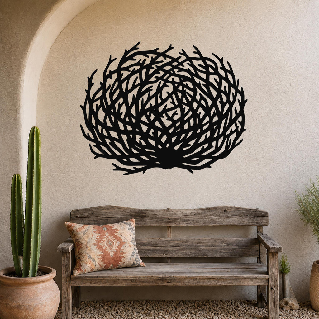 Black metal wall art in a circular tumbleweed silhouette with intricate branch cutouts, mounted on a textured wall above a rustic wooden bench in a desert boho-style entryway.
