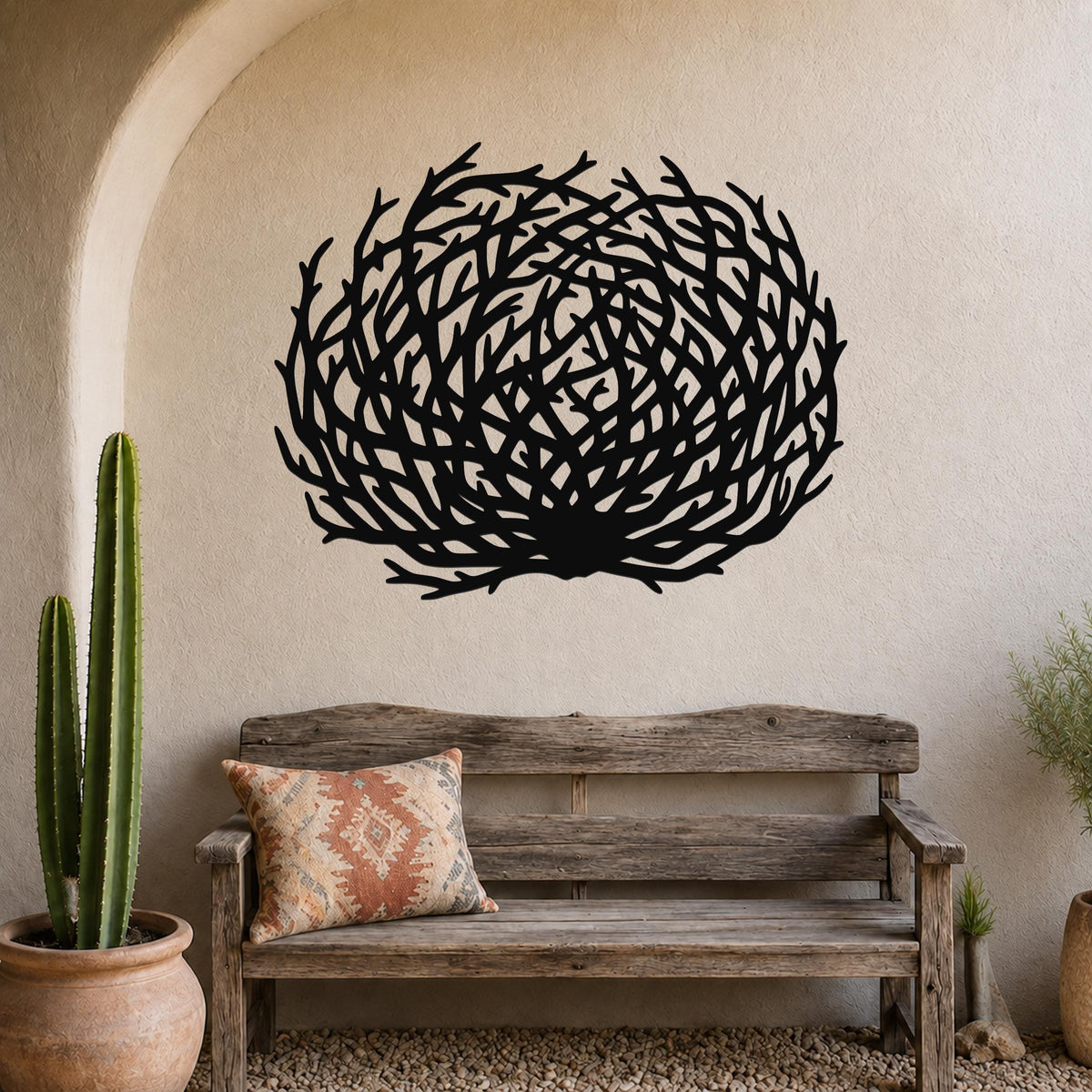 Black metal wall art in a circular tumbleweed silhouette with intricate branch cutouts, mounted on a textured wall above a rustic wooden bench in a desert boho-style entryway.