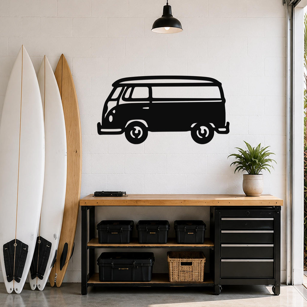 Black metal wall art cutout of a vintage van with surfboard on roof, mounted on a white brick wall above a wooden workbench in a garage.