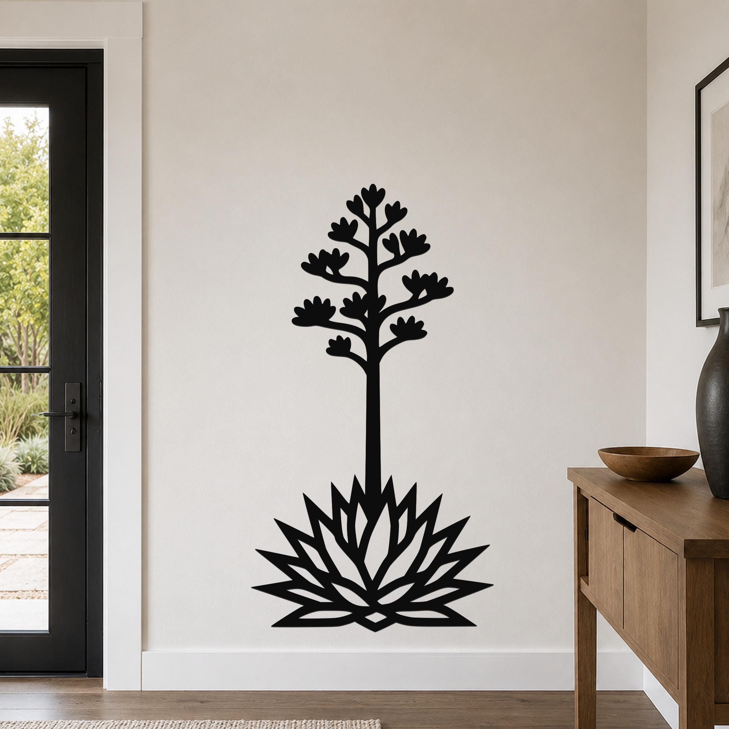 Black metal wall art silhouette of a blooming agave with a tall stem, flower clusters, and spiky base, mounted on a light-colored wall in a modern entryway.