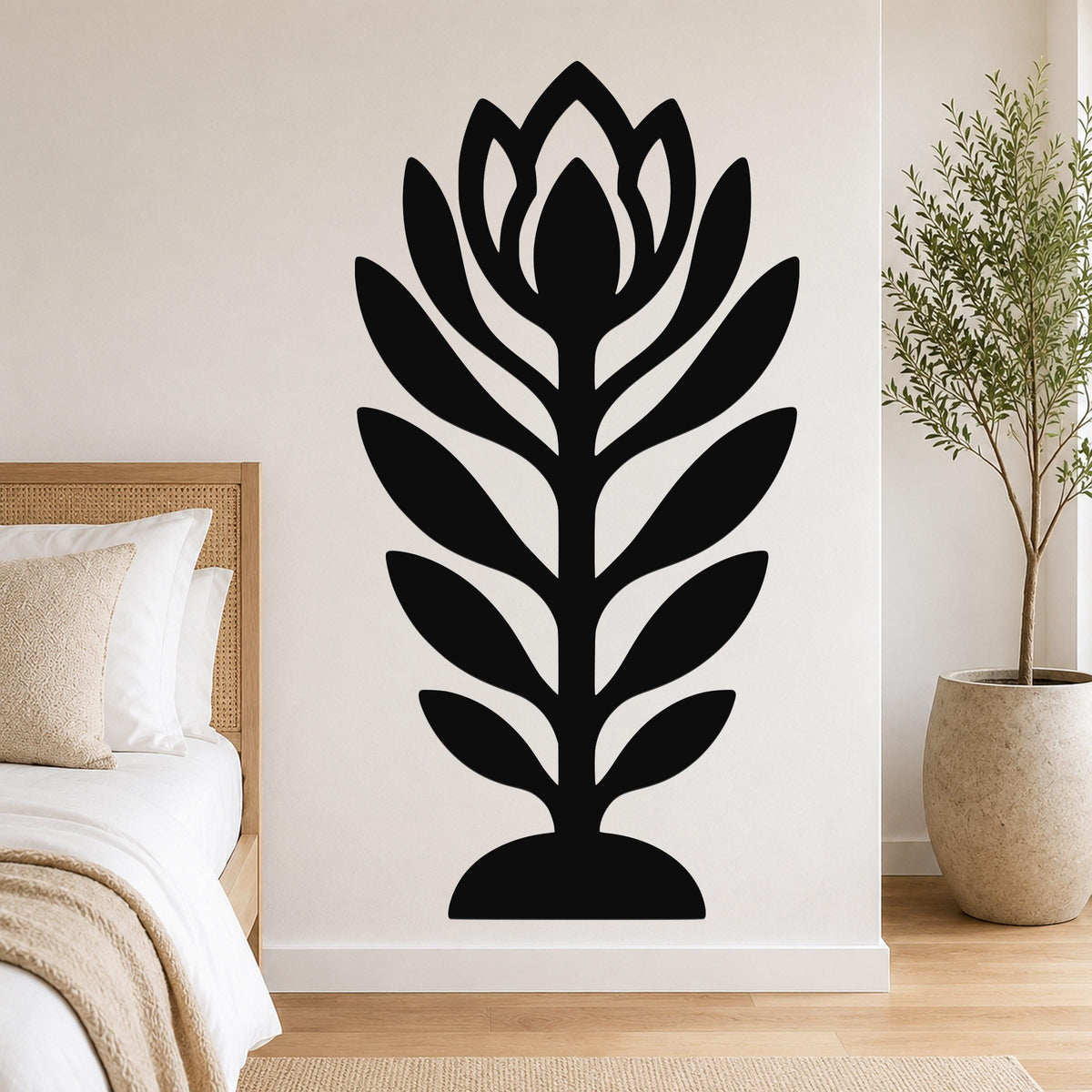Black metal wall art in a stylized wildflower silhouette with layered petals and leaves, mounted on a bedroom wall above a bed.