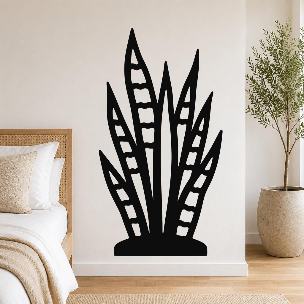 Black metal wall art in the shape of a snake plant with internal cutout details, mounted on a bedroom wall above a bed.