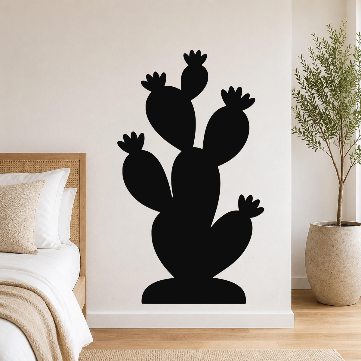 Black metal cactus wall art with multiple paddle-shaped arms and flower cutouts, mounted on a white bedroom wall above a bed.
